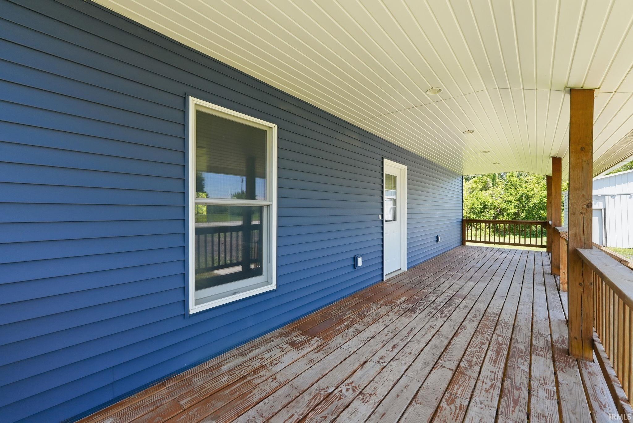 Expansive covered porch featuring a wood deck, wood railings, and wood support columns