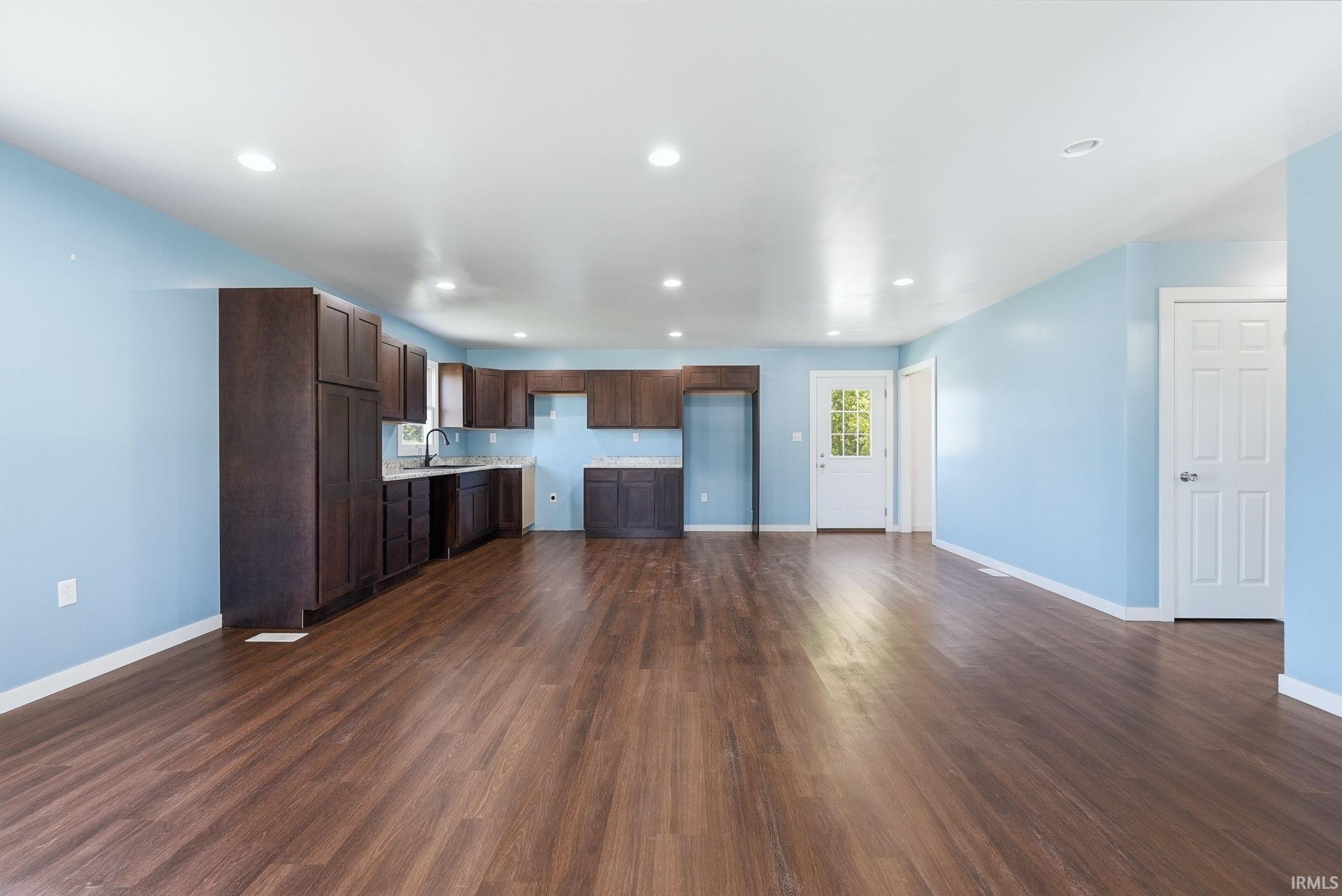 Spacious open-concept interior featuring wood-finish flooring, recessed lighting, and a kitchen area with dark wood cabinetry
