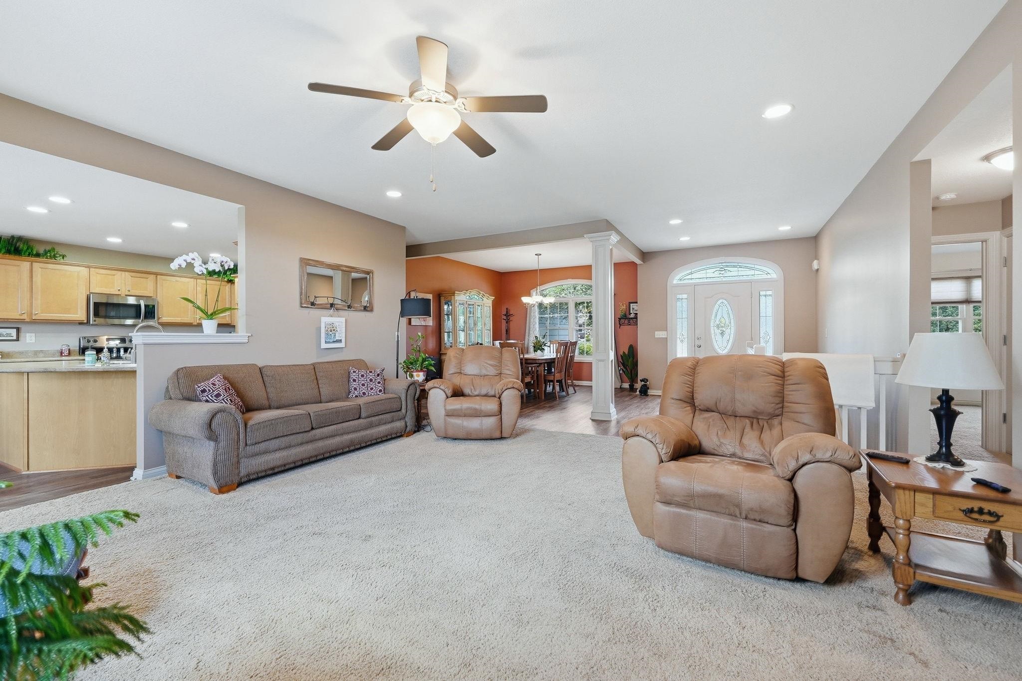 Carpeted living area featuring a ceiling fan, recessed lighting, and a view into the kitchen with wood cabinetry and stainless steel appliances