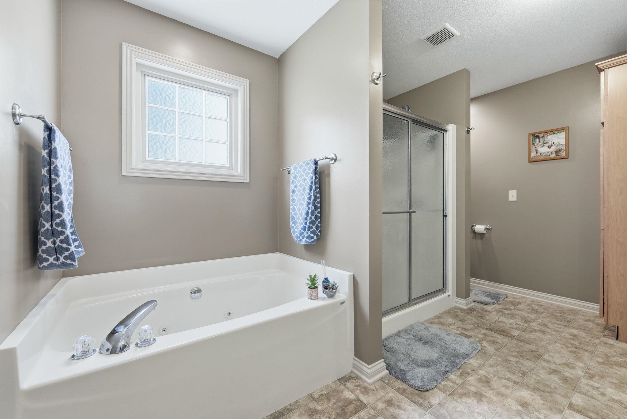 Bathroom featuring a built-in soaking tub with chrome fixtures, a frosted window, a separate shower enclosure with sliding glass doors, and a wood-finish floor