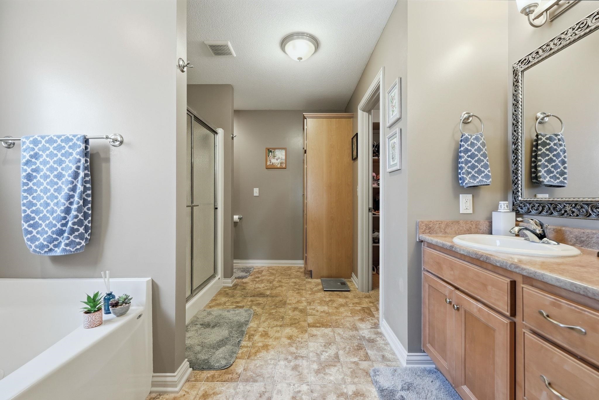 Bathroom featuring a built-in bathtub, a shower with a clear glass enclosure, and a vanity with wood-finish cabinetry, a built-in sink, and an ornate framed mirror