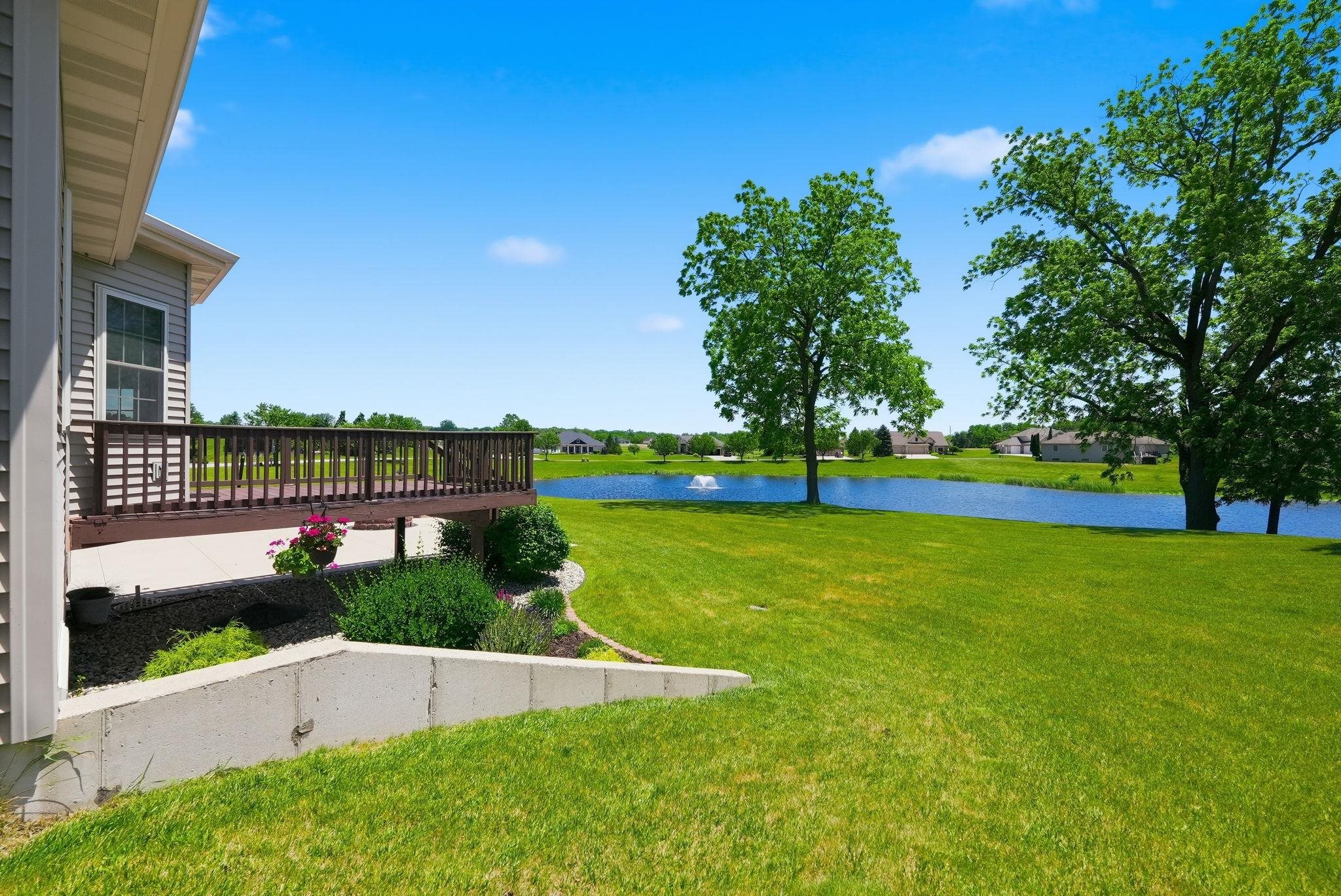 Expansive backyard featuring a large green lawn, mature trees, a private wooden deck, and a retaining wall