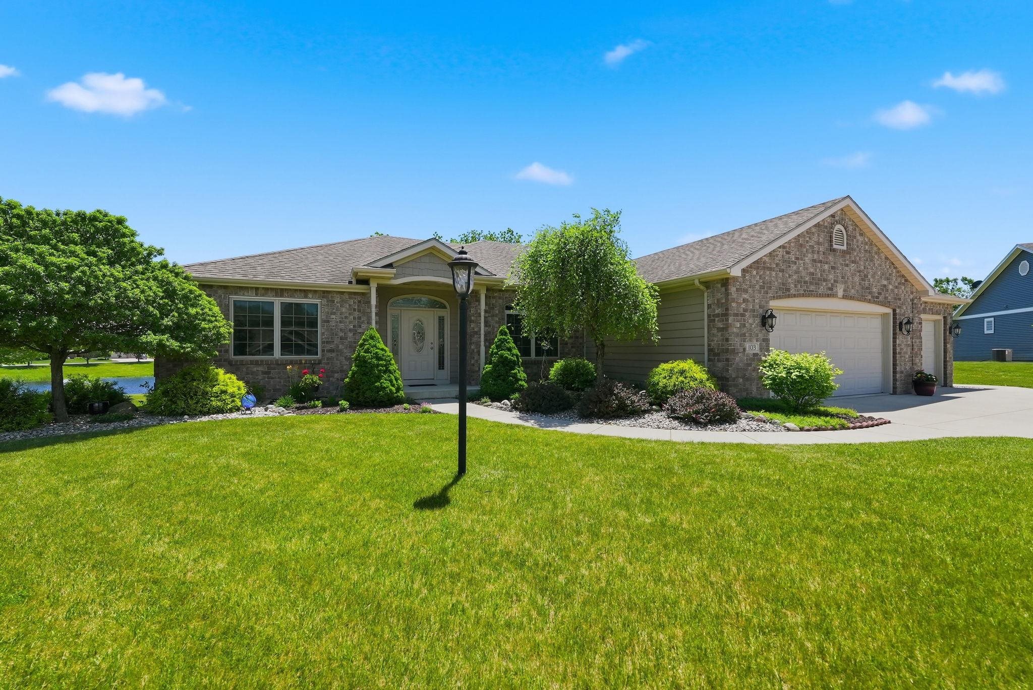 Ranch-style residence featuring a brick and siding exterior, a prominent two-car garage with arched entrances, a paved driveway, and established landscape plantings