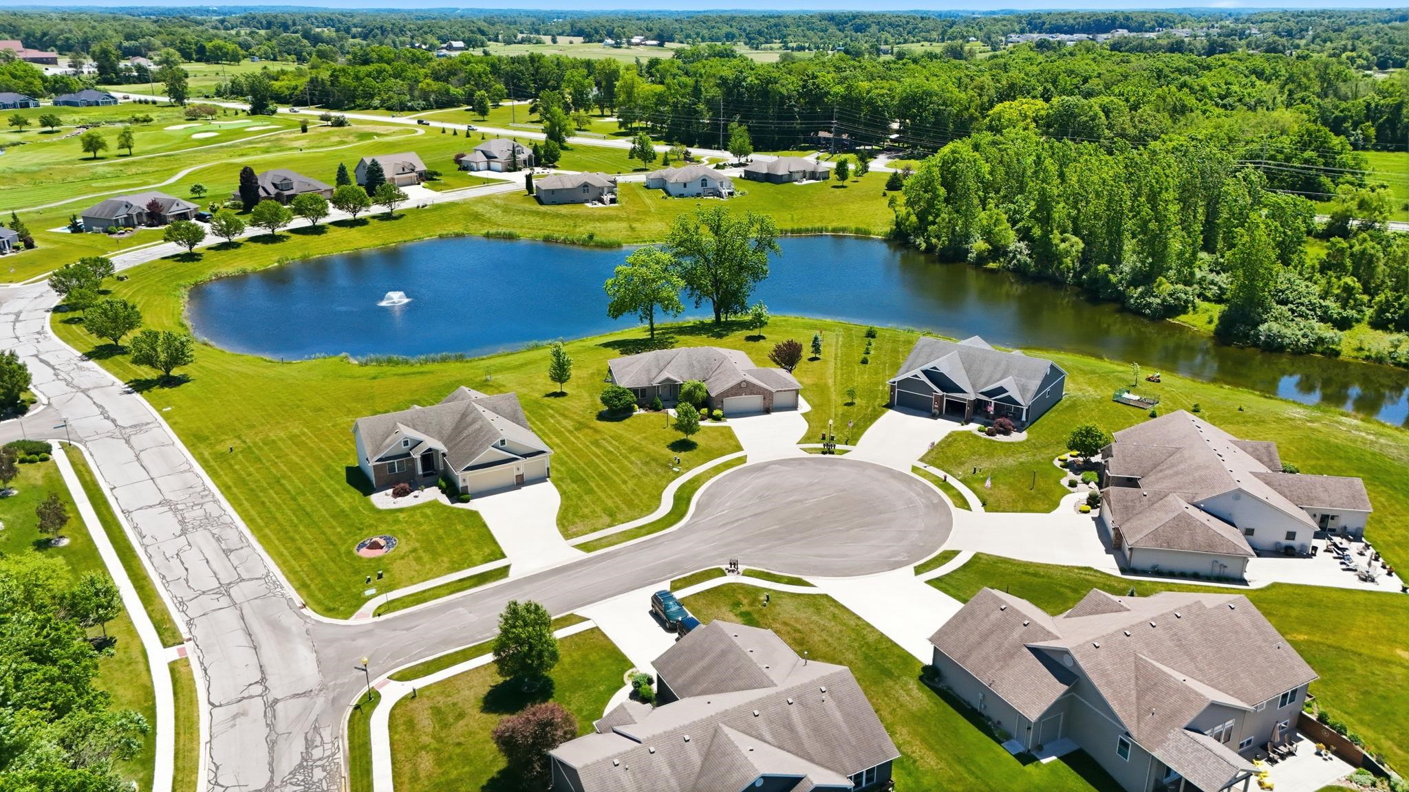Expansive neighborhood featuring a large pond with a water feature, surrounding lush green landscaping, and numerous mature trees