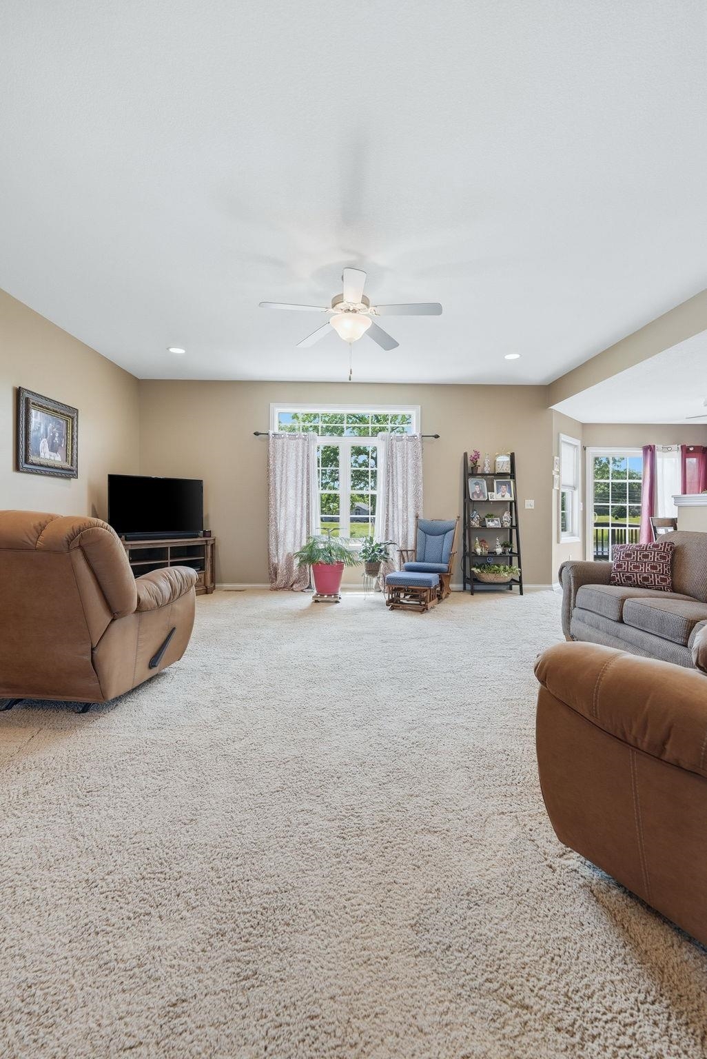 Spacious living area featuring neutral-toned walls, plush carpeting, a ceiling fan with integrated lighting, recessed lighting, and large windows with transom detailing