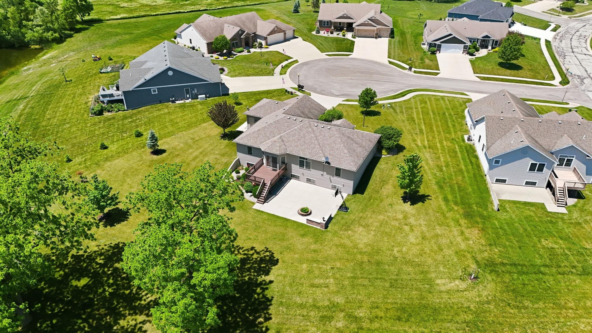 Expansive property featuring a concrete patio, wood deck, mature trees, and a sloped lawn