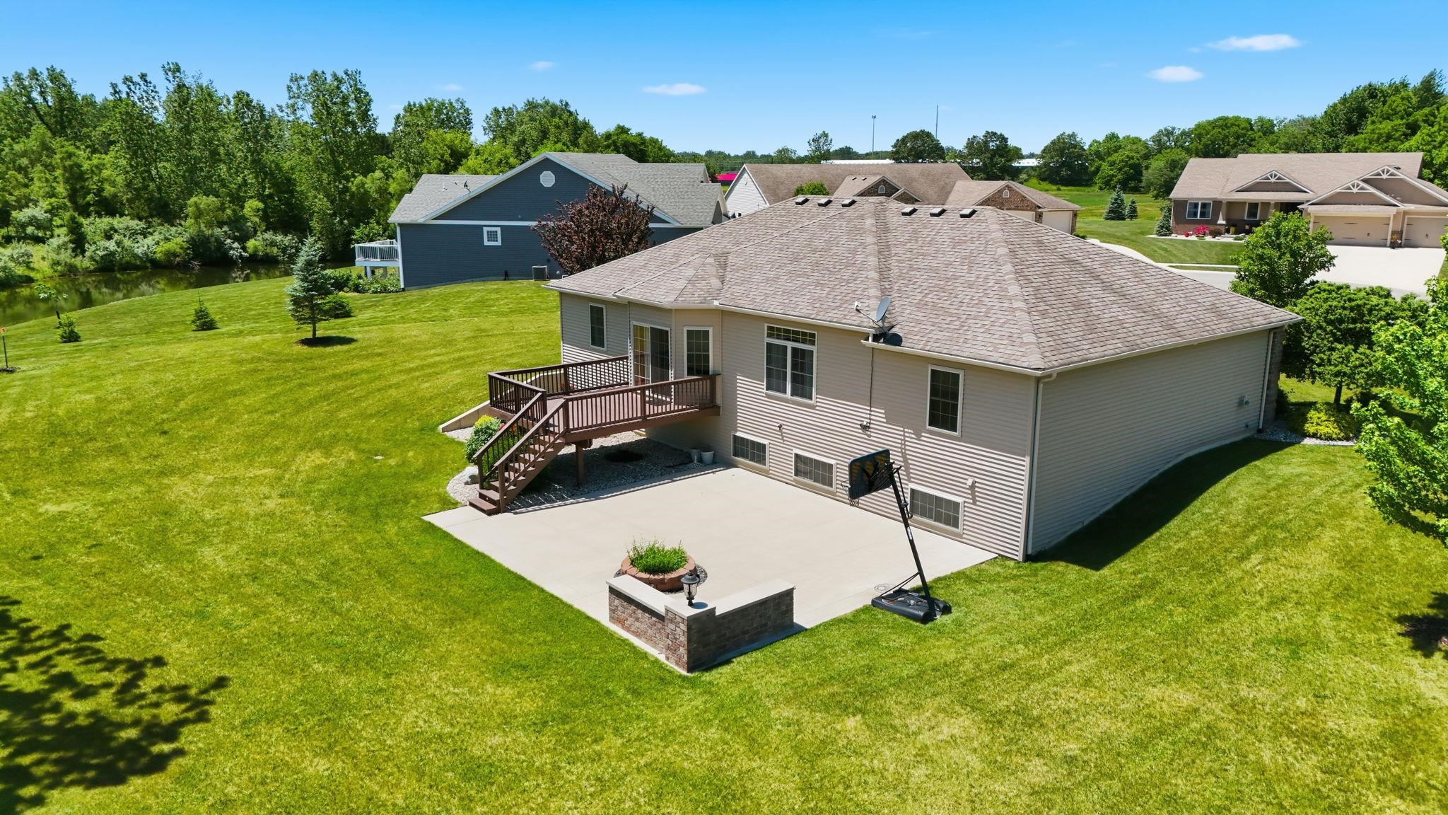 Expansive rear yard featuring a concrete patio, wood deck with stairs, and mature landscaping