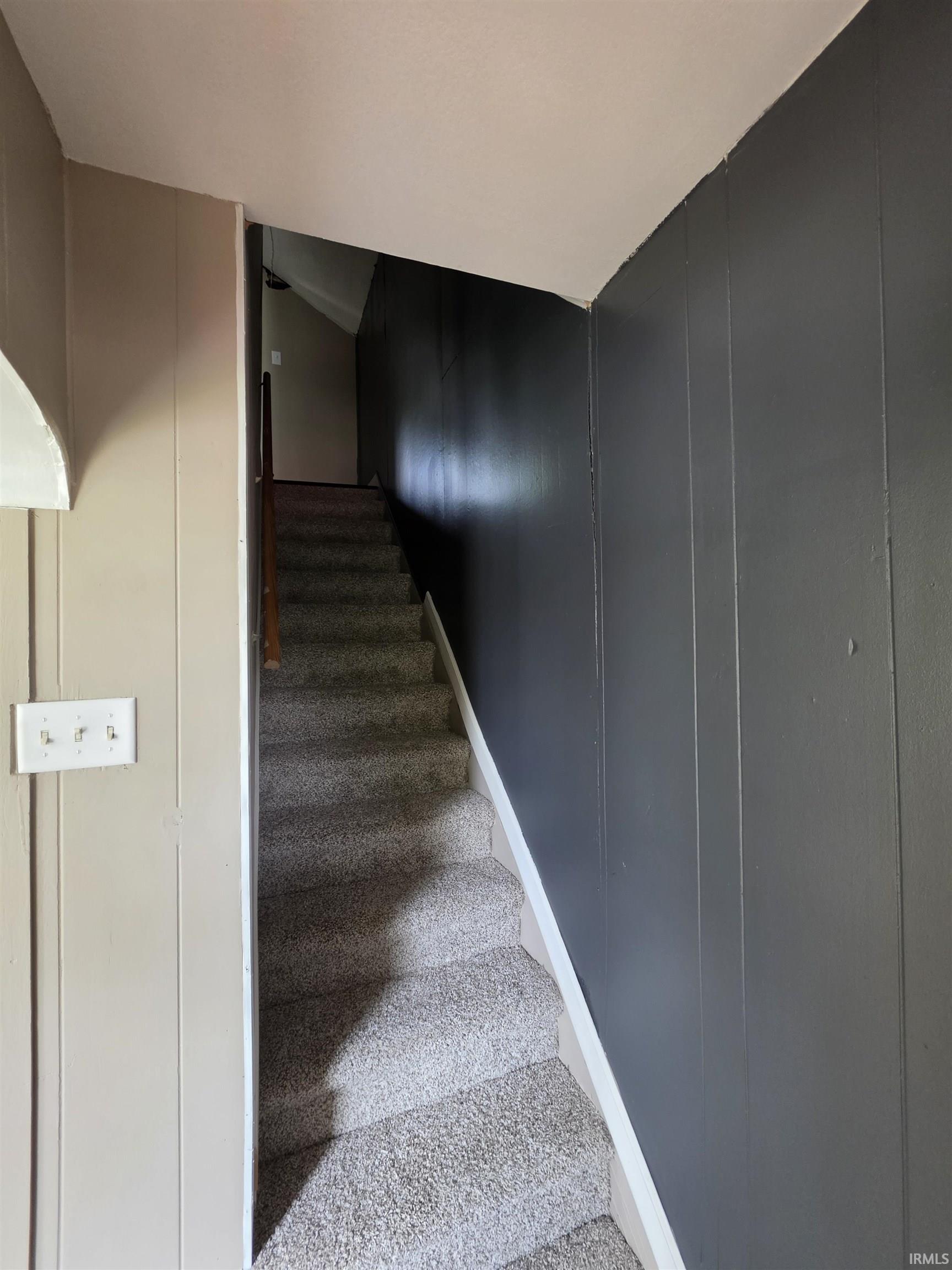 Carpeted staircase featuring a light gray wall paneling, dark gray wall paneling, white trim, and a wood handrail