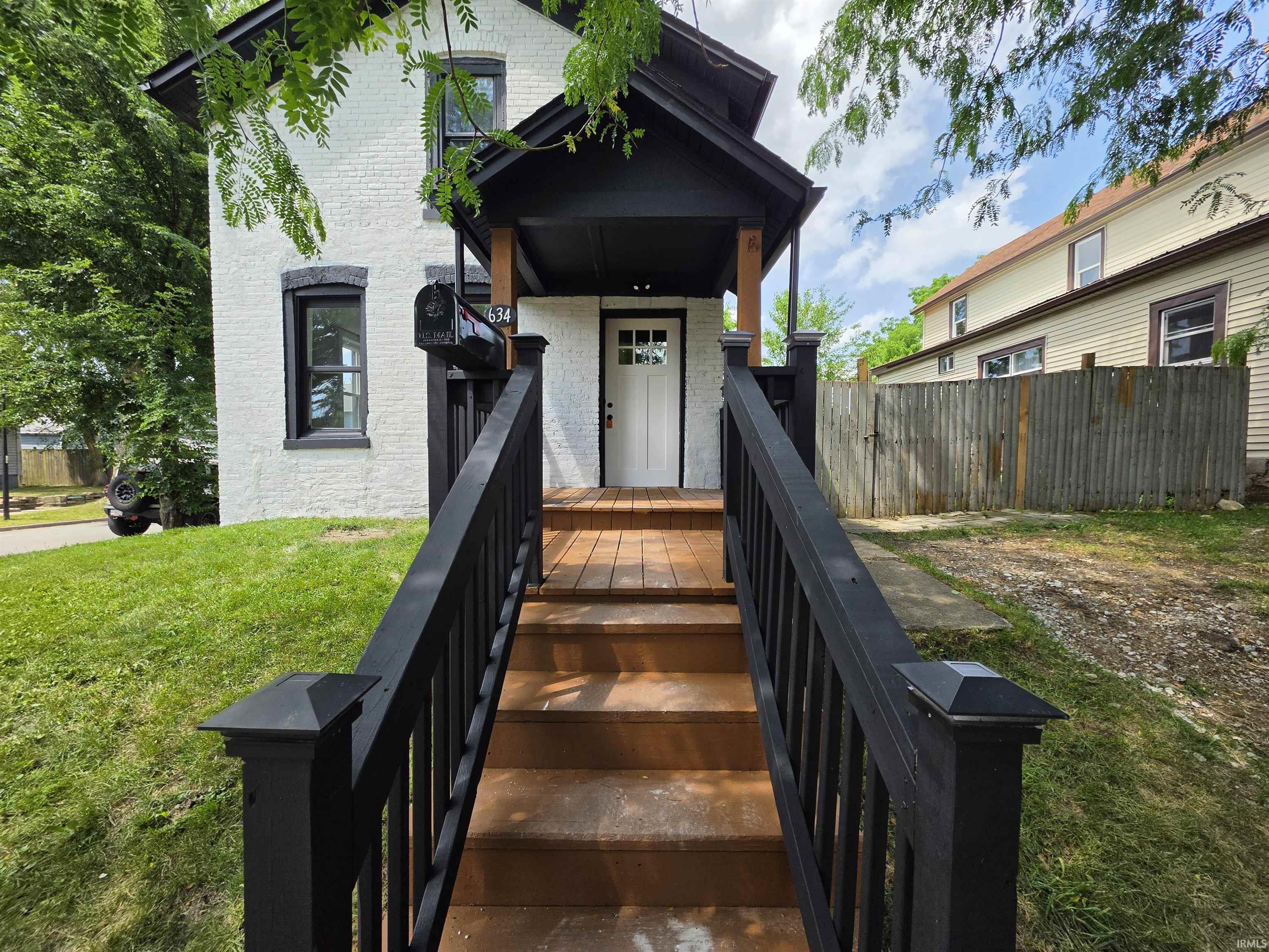 White brick exterior with dark trim, featuring a covered porch and wood-finish steps