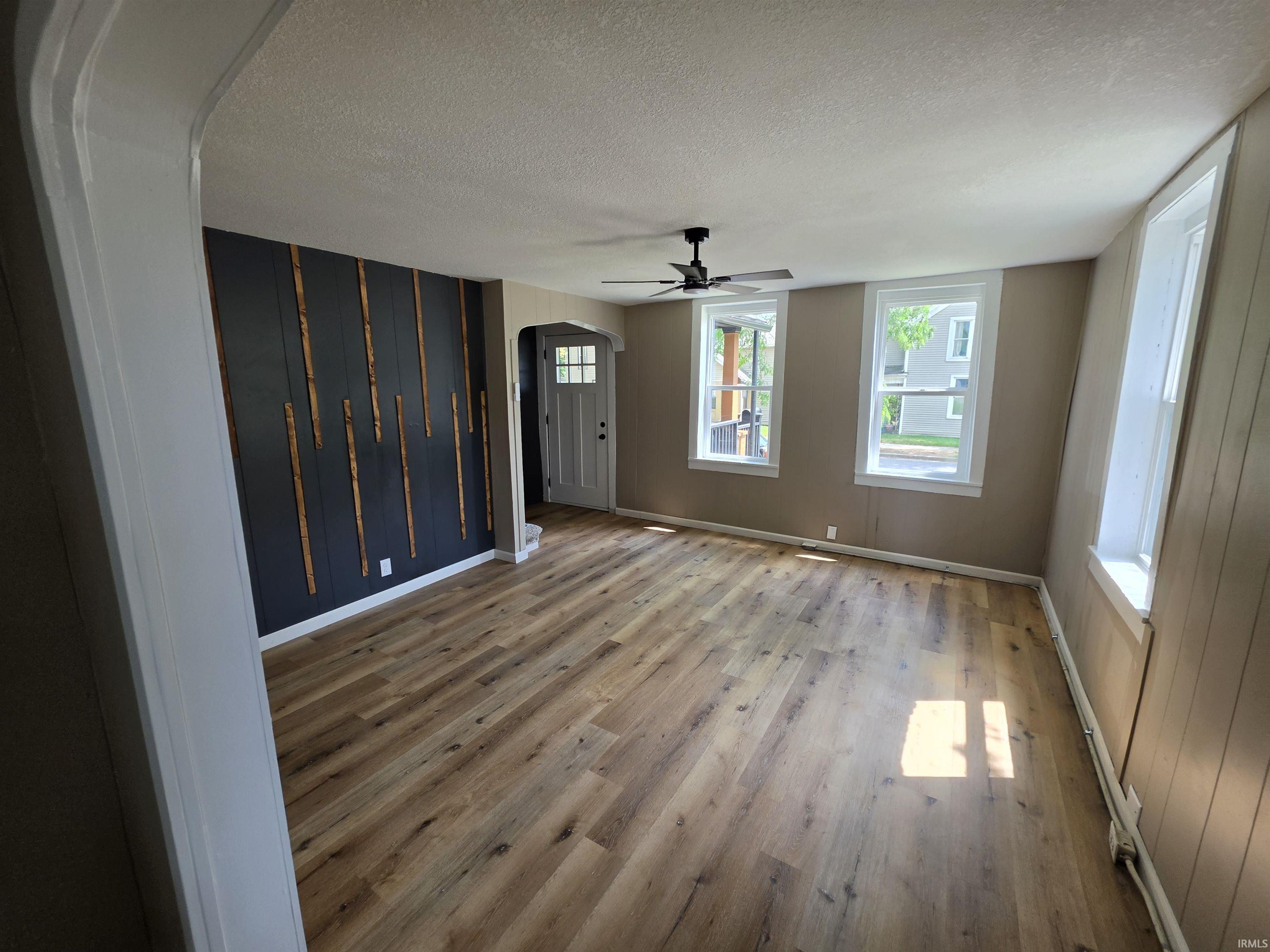 Spacious interior room featuring wood-finish flooring, a contemporary accent wall with vertical wood elements, and multiple windows providing natural illumination