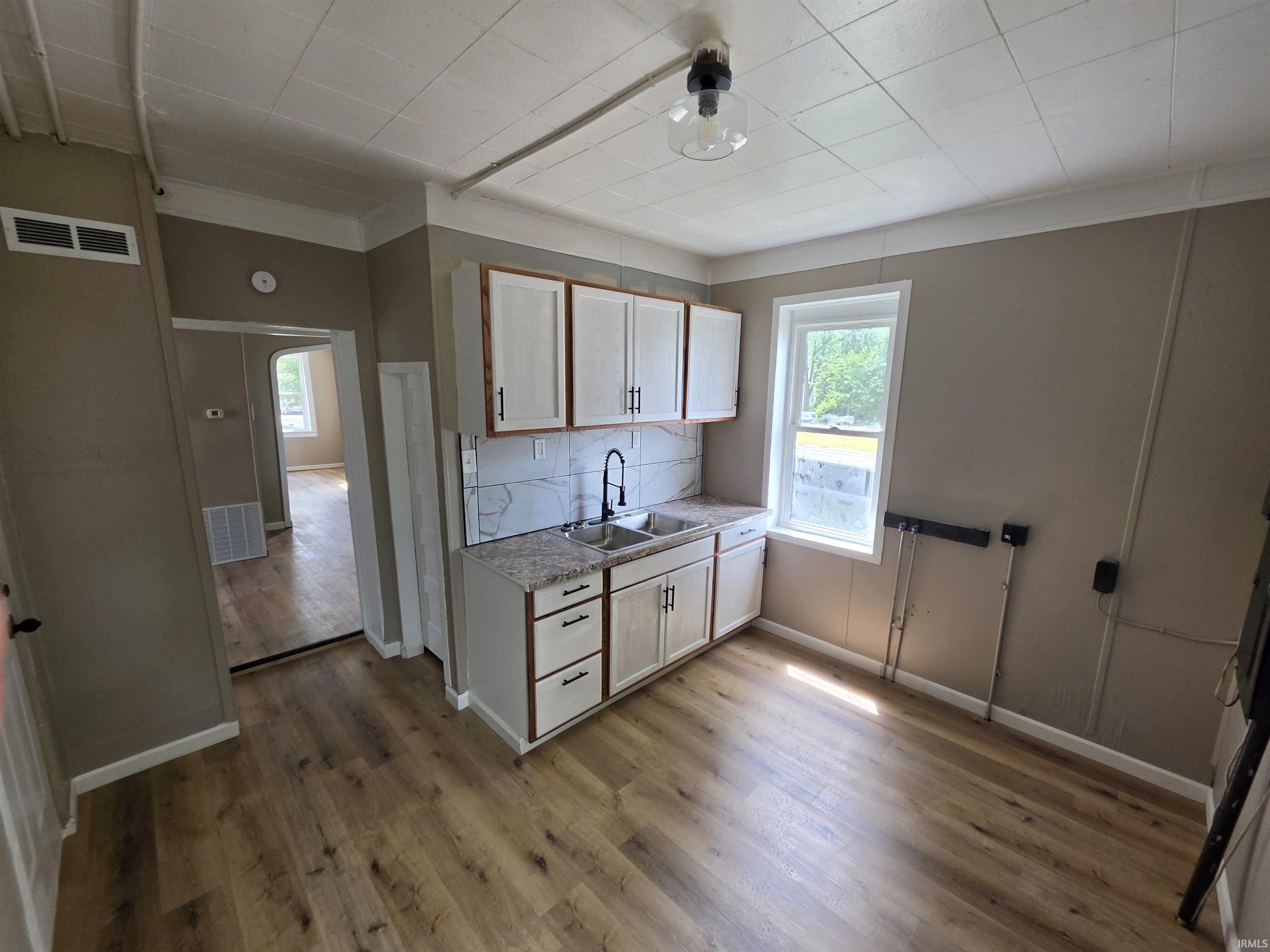 Kitchen featuring wood-finish flooring, white cabinetry with dark hardware, a double basin sink with a matte black faucet, and a tile backsplash