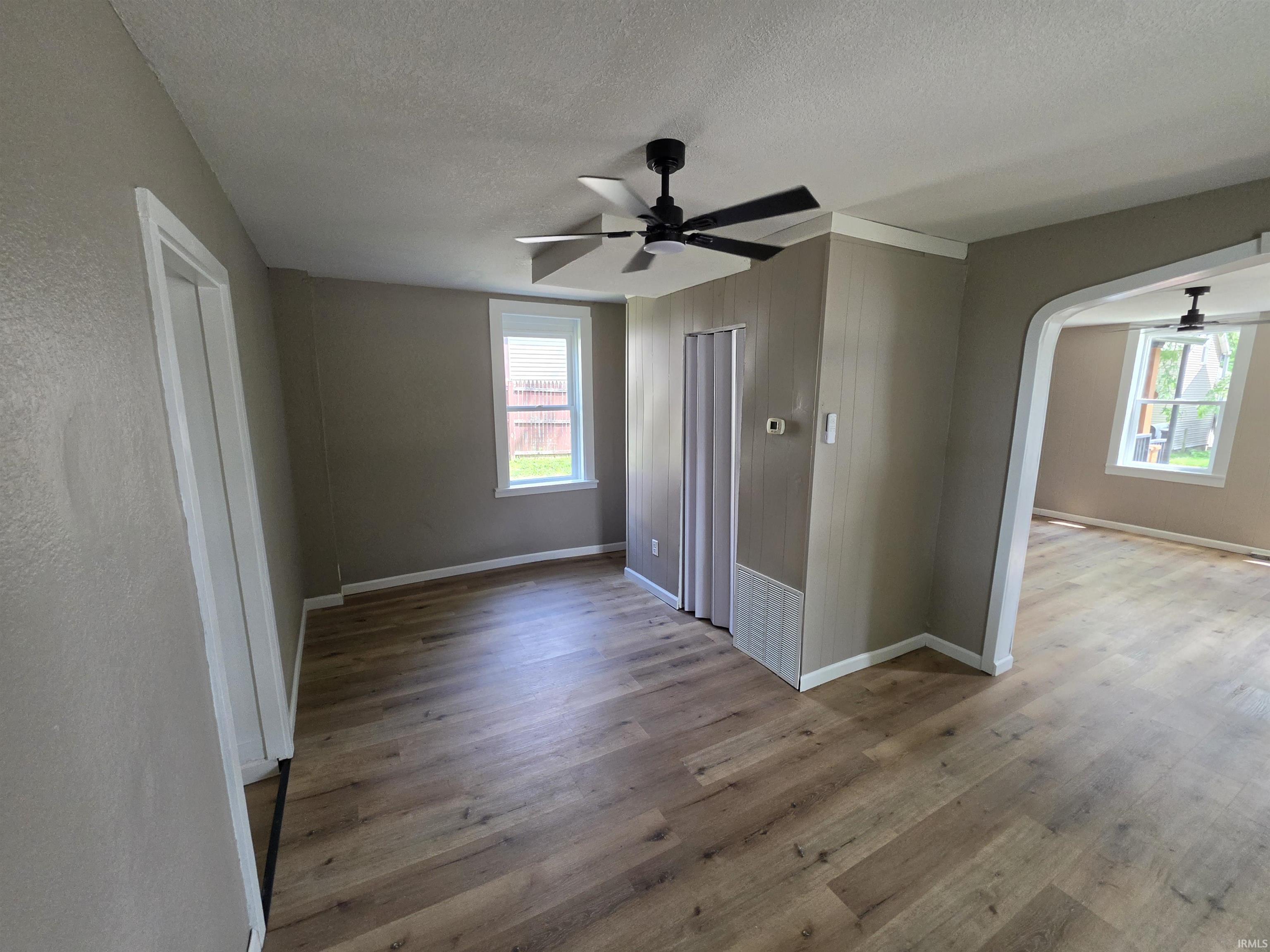 Spacious interior room featuring wood-finish flooring, a contemporary ceiling fan, and multiple windows with white trim