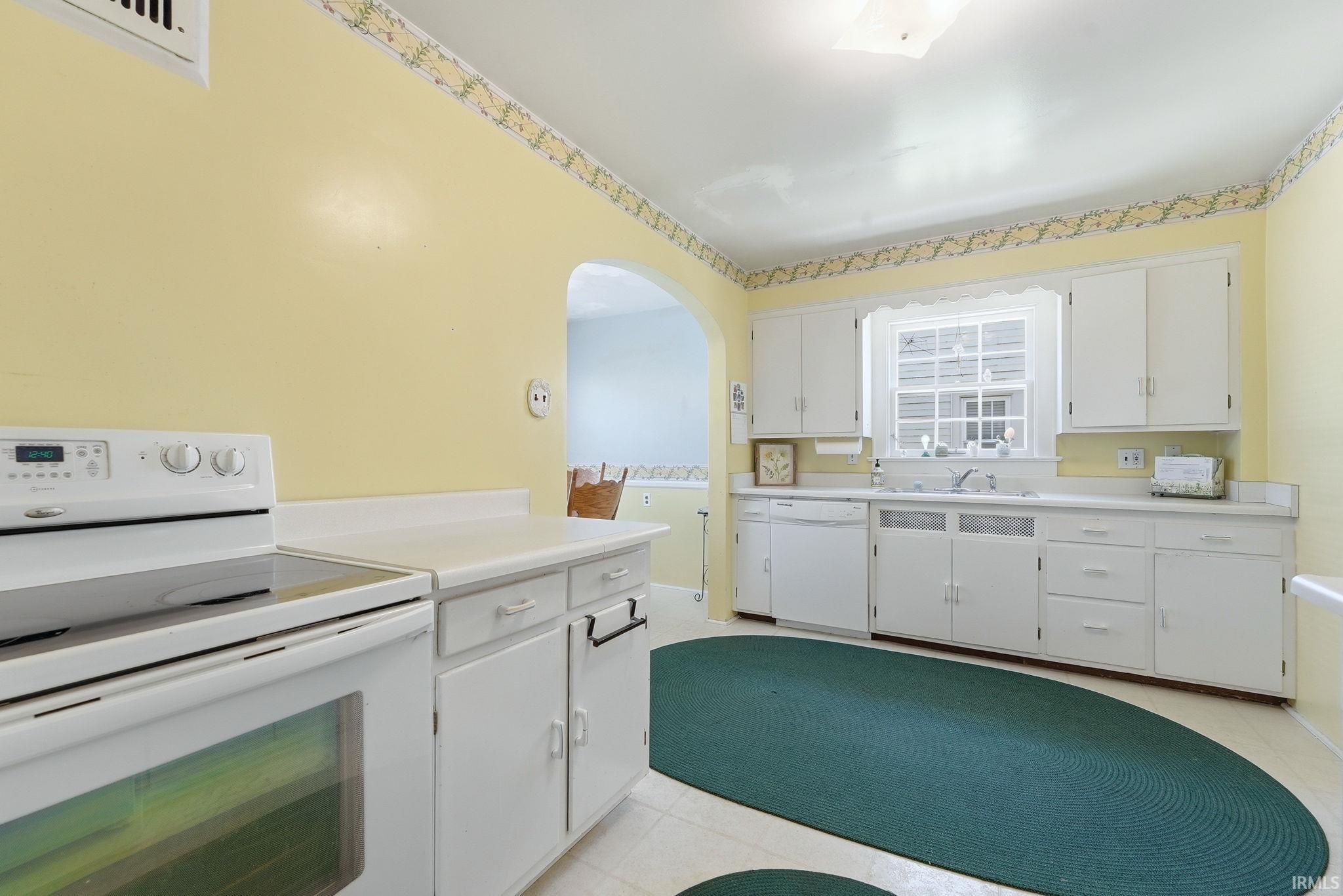 Bright kitchen featuring white cabinetry, a single basin sink under a window, white appliances, and a coved archway