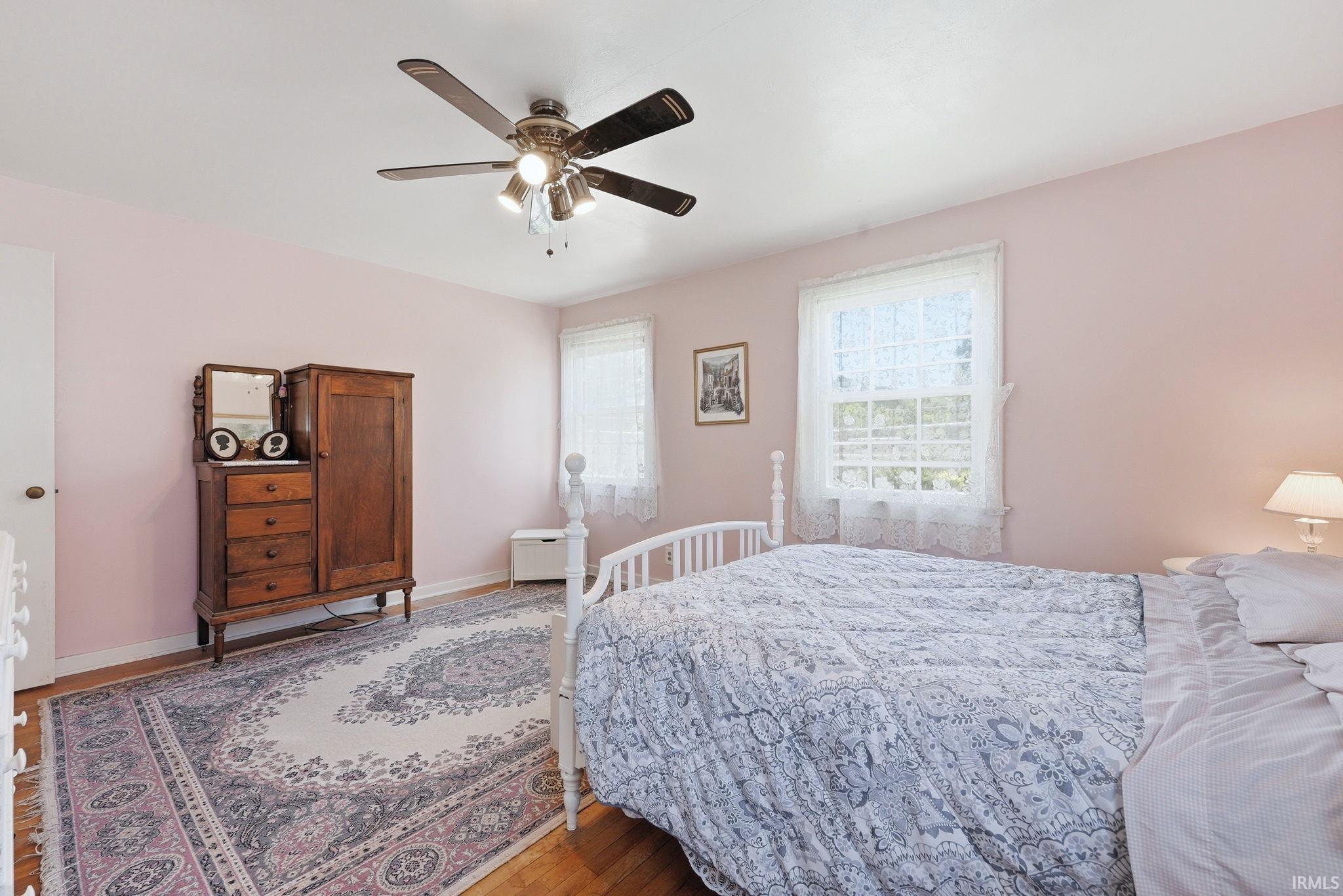 Bright room featuring two windows, wood-finish flooring, and a ceiling fan with integrated lighting