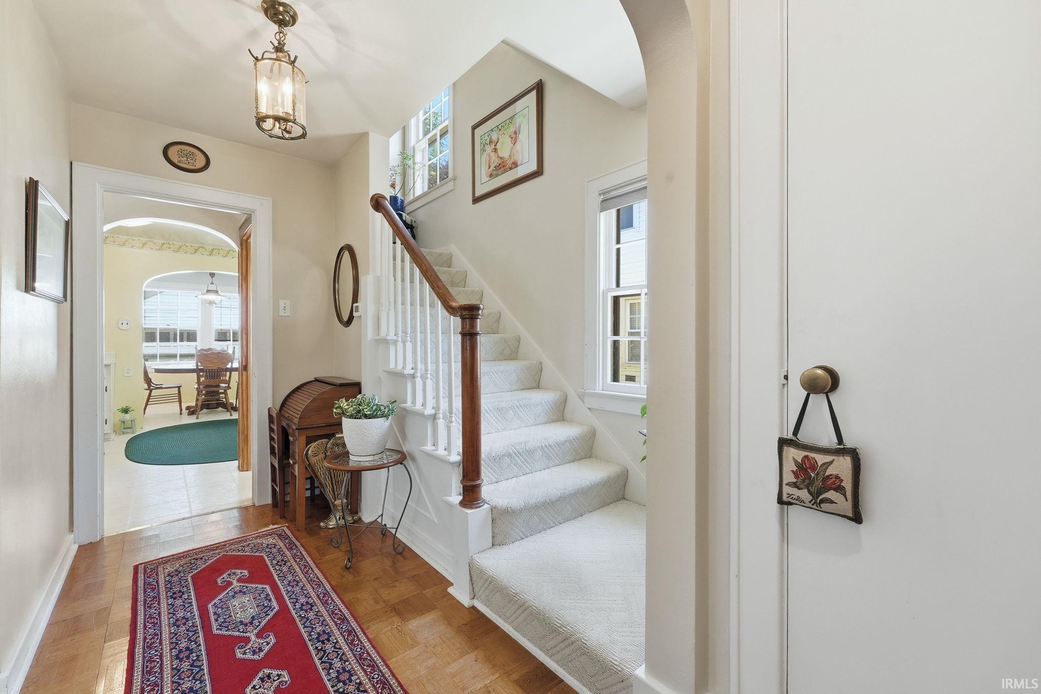 Foyer featuring wood-finish flooring, a carpeted staircase with white balusters and a wood handrail, an arched doorway, and an overhead lantern-style light fixture