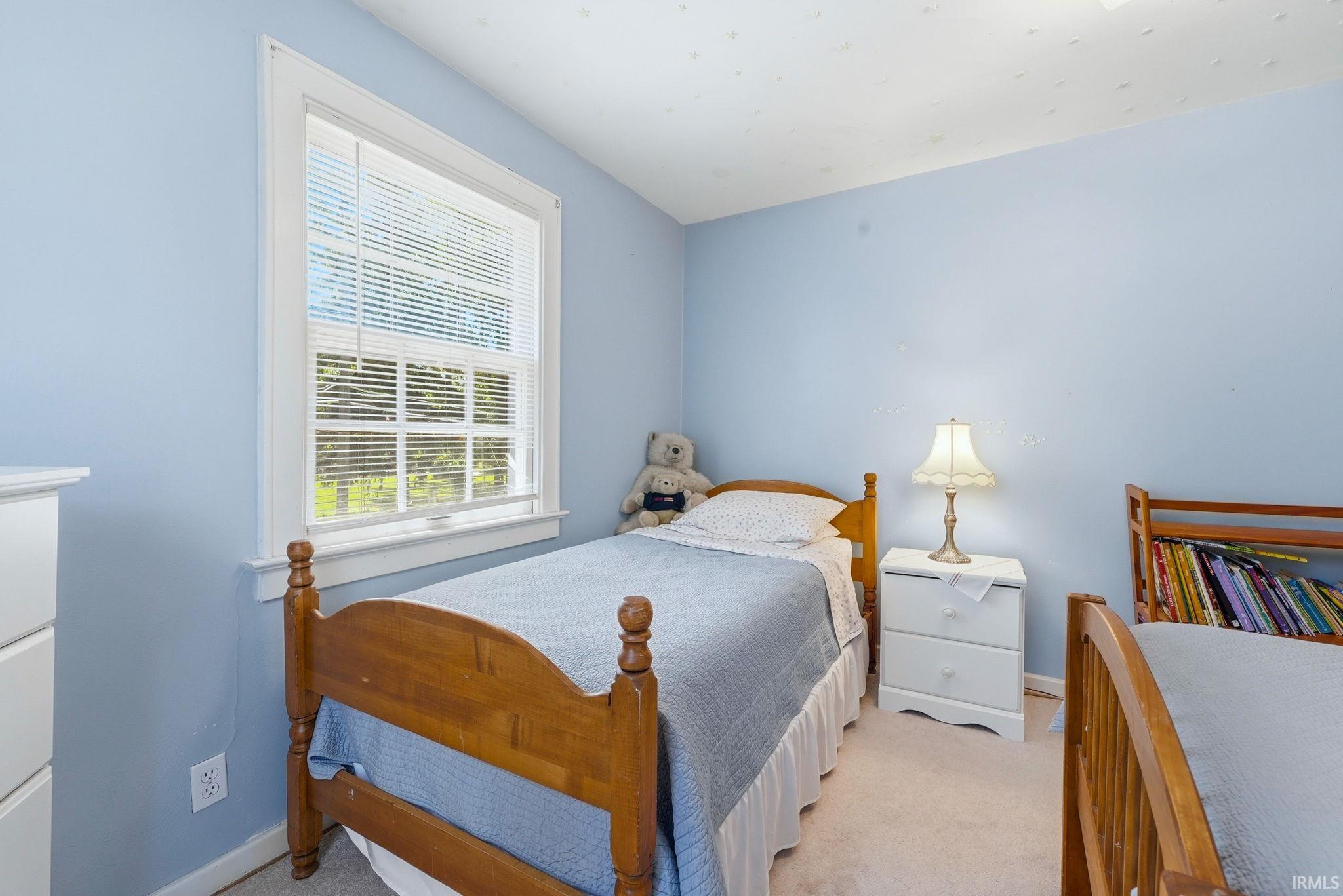 Bedroom featuring a double-hung window with white blinds, light blue walls, and neutral carpet flooring