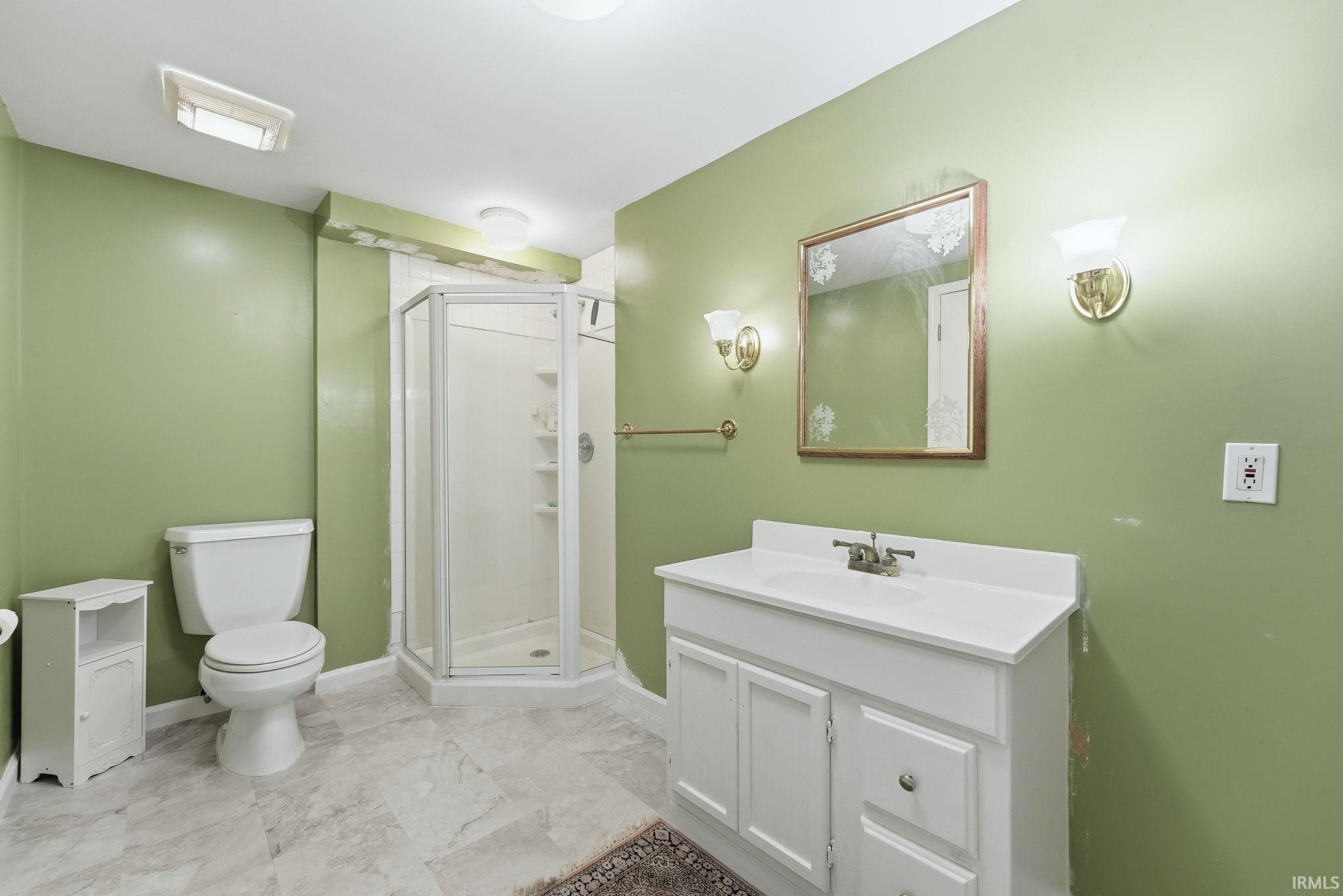 Bathroom featuring a corner shower with glass enclosure, single vanity with white countertop, wall-mounted mirror, and tile flooring