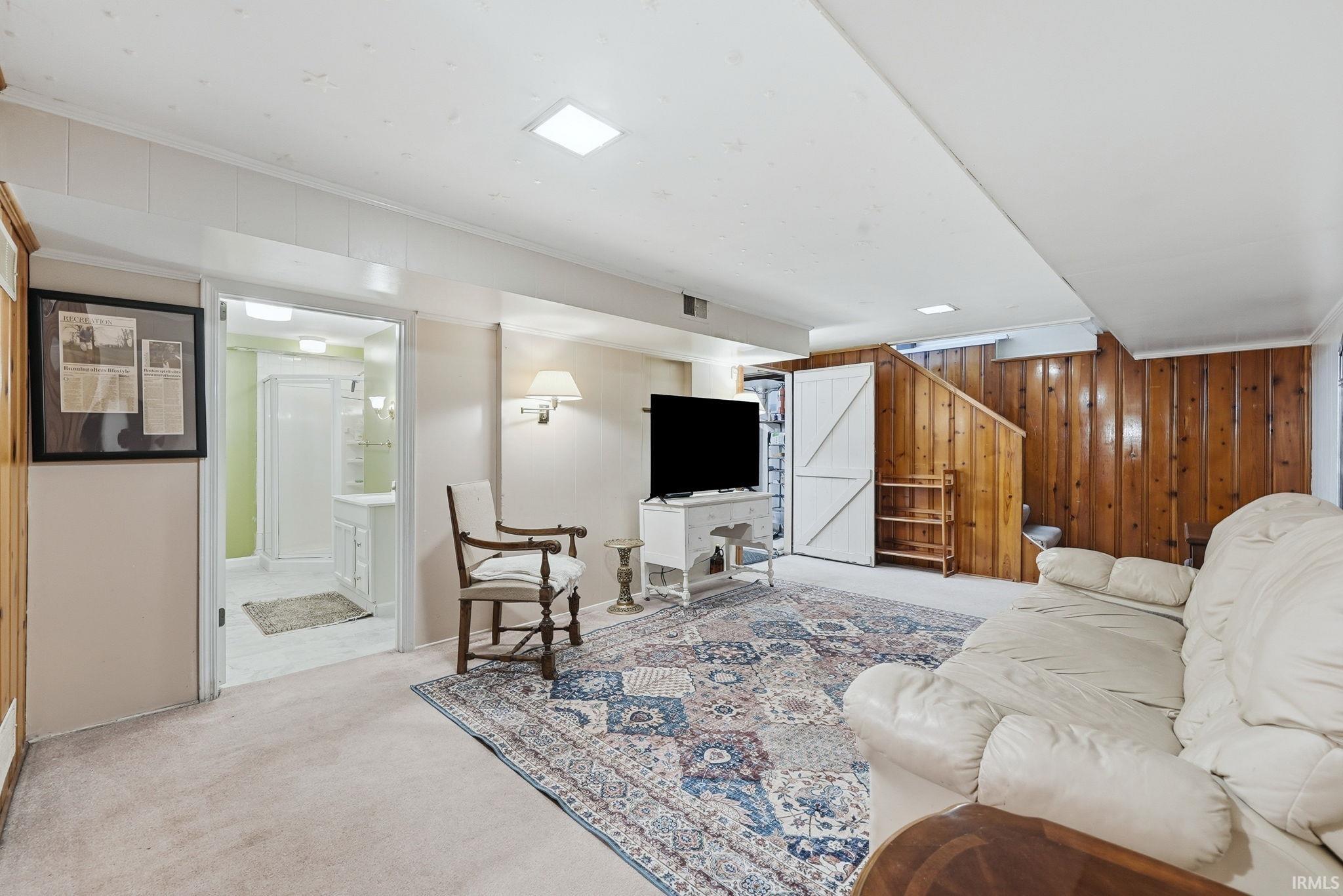 Carpeted recreational room featuring wood paneling, recessed lighting, and access to a full bathroom and laundry room.