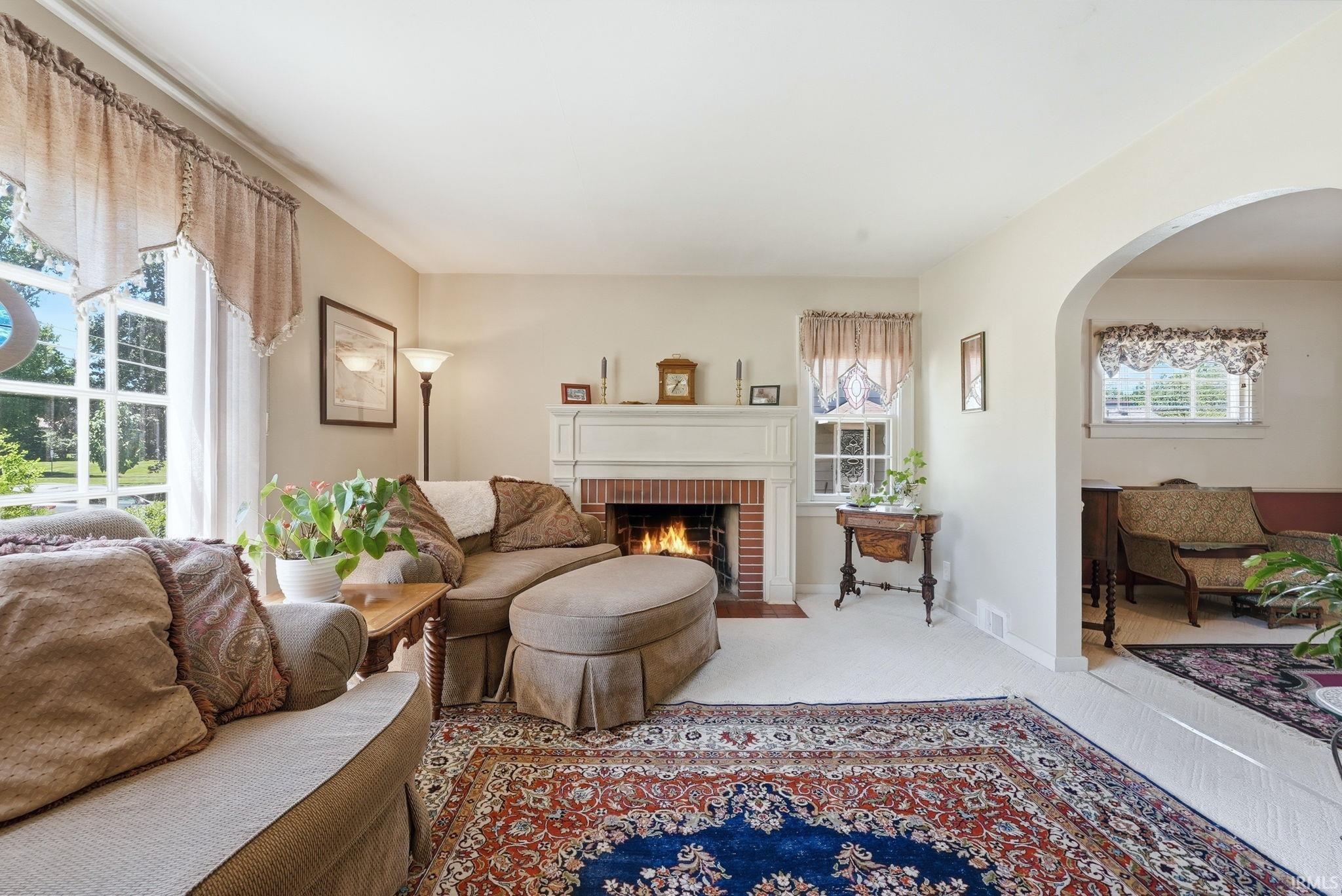 Living area featuring a brick fireplace with a white mantel, large windows, an arched doorway, and light-colored wall paint
