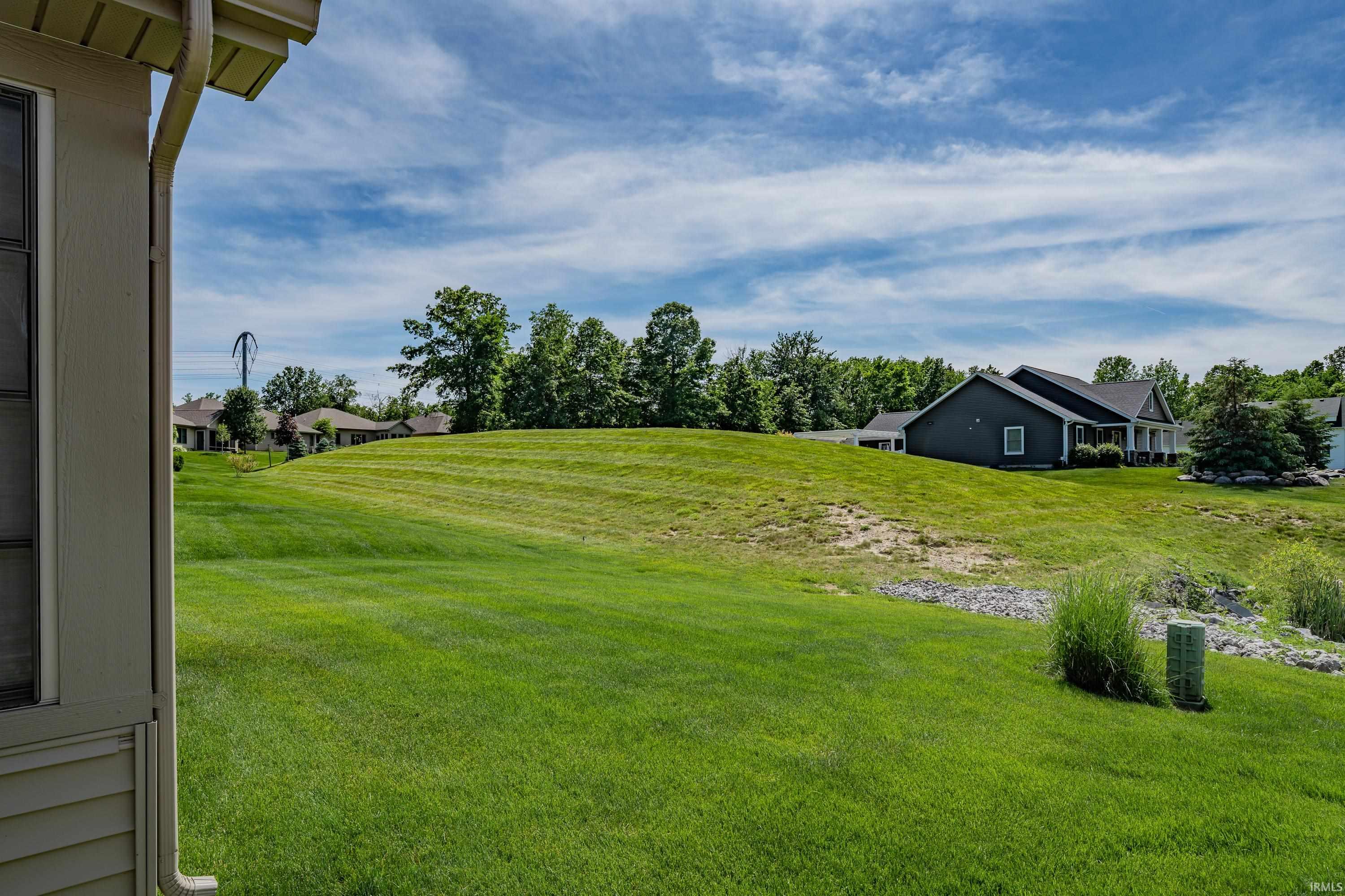 Expansive grassy slope with distant residential structures and mature trees