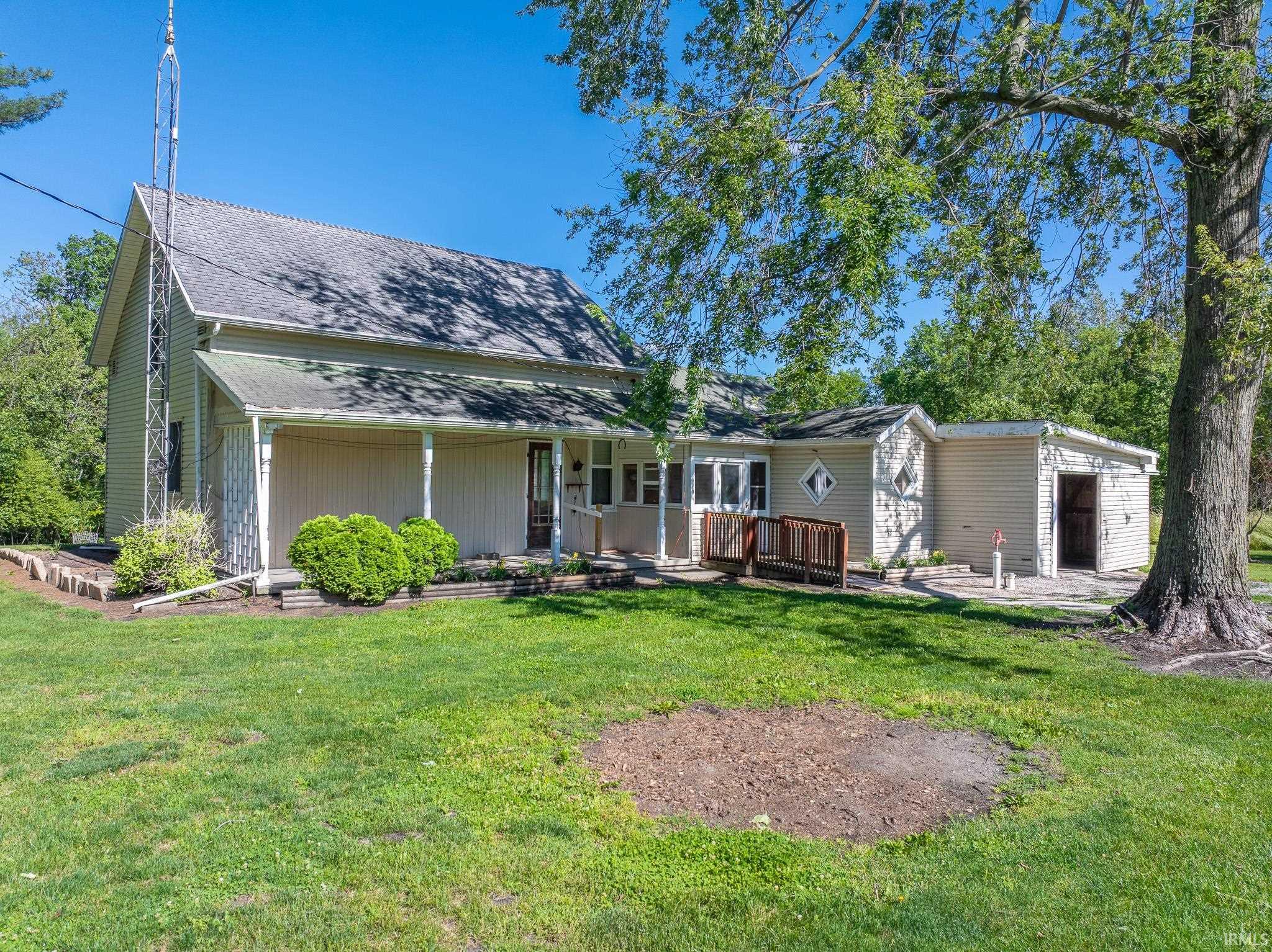 Exterior residence featuring light-colored siding, an attached covered porch, a separate utility structure, and mature trees on a grassy lot