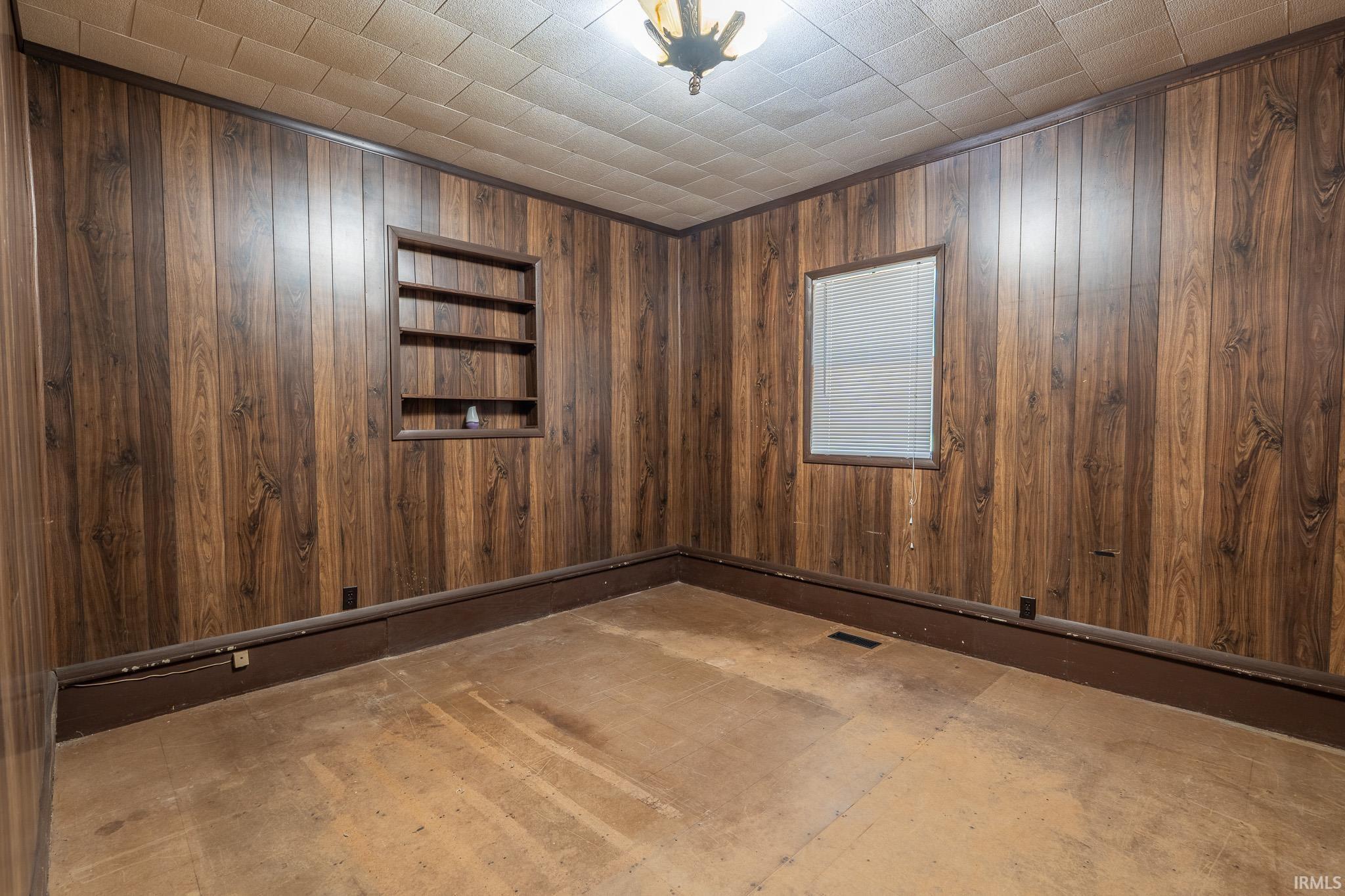Room featuring wood-finish wall paneling, built-in shelving, a single window, a textured ceiling, and baseboard trim