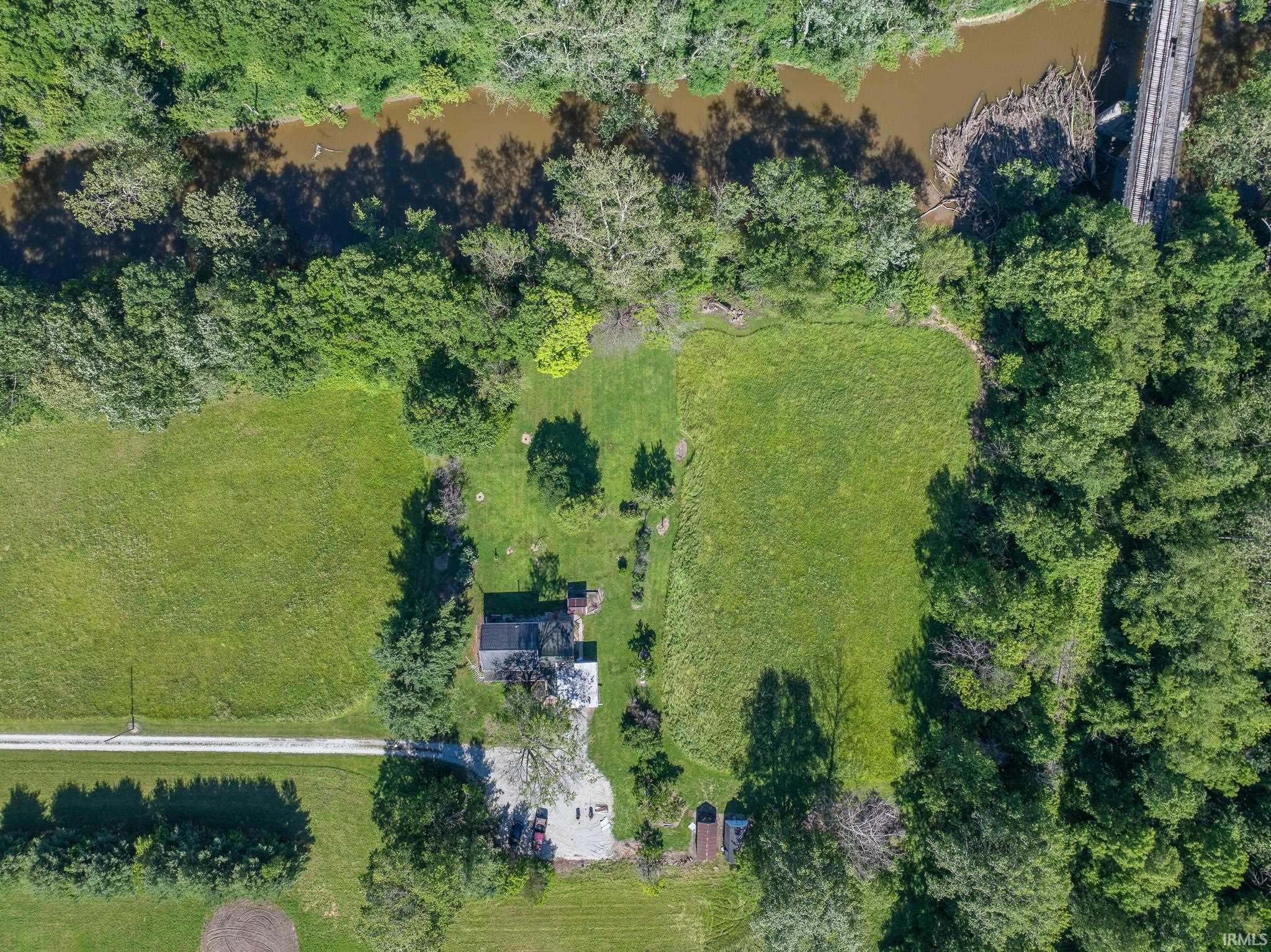 Expansive property featuring a single-story residence, gravel driveway, surrounding green spaces, mature trees, and a bordering river with a bridge structure