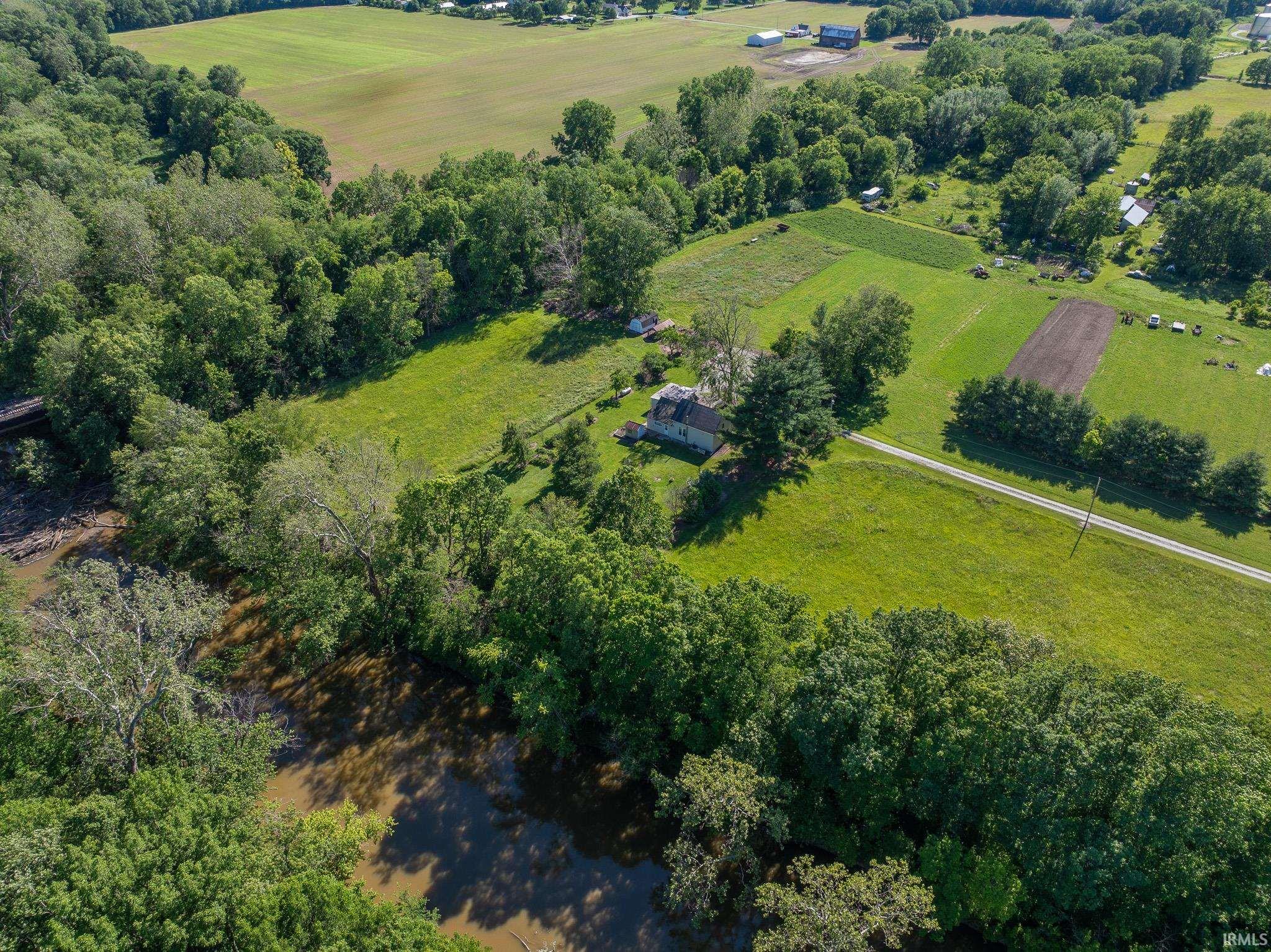 Expansive land parcel featuring a single-story dwelling, mature trees, open fields, a visible river, and a private access road