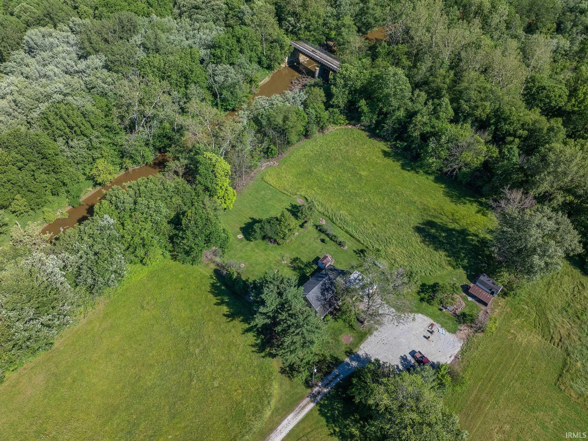 Expansive property featuring a gravel driveway, a single-story residence with a dark roof, surrounding green lawns, and mature trees