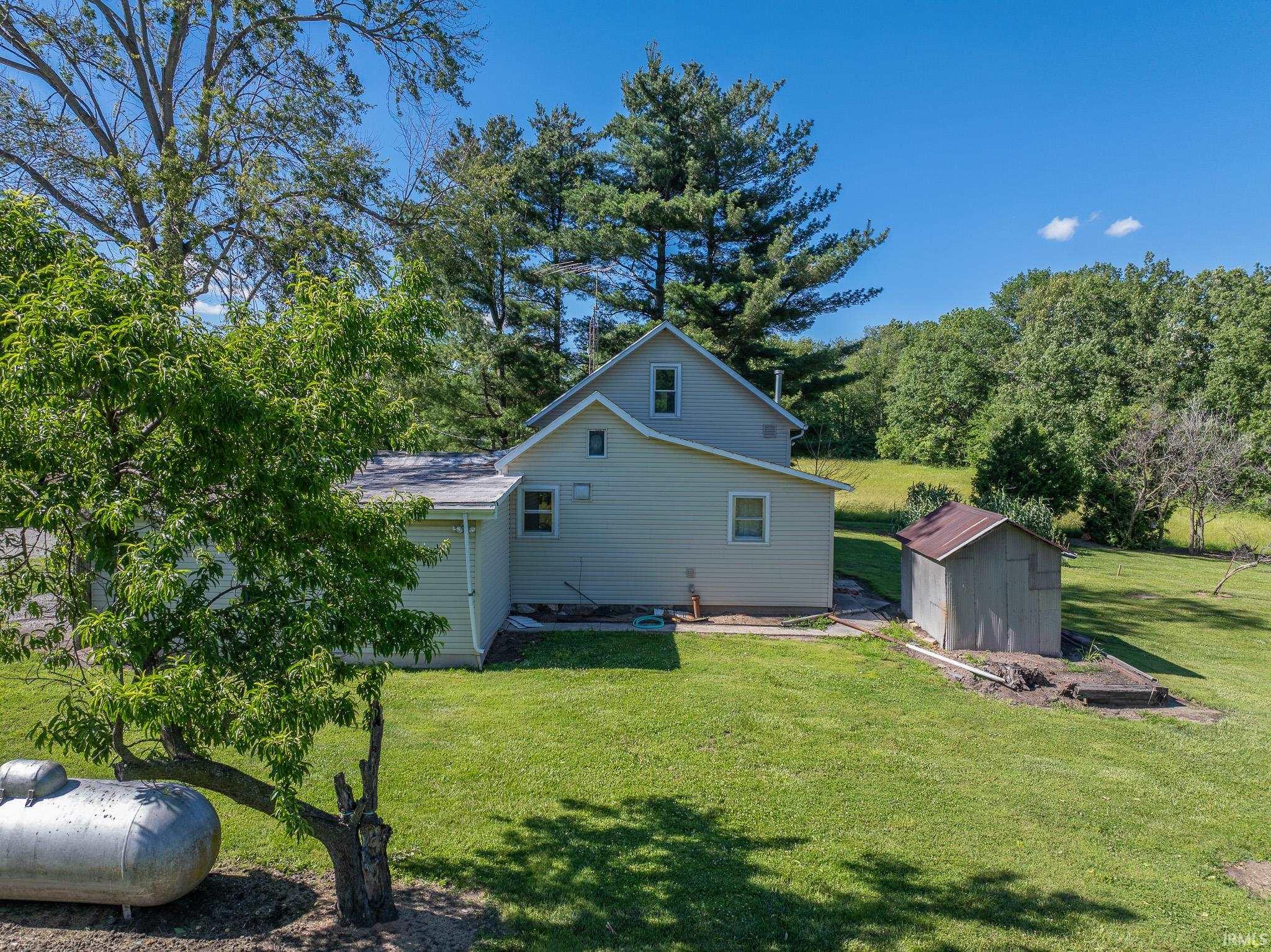 Spacious exterior featuring light-colored siding, a detached storage shed, mature trees, and a well-maintained lawn