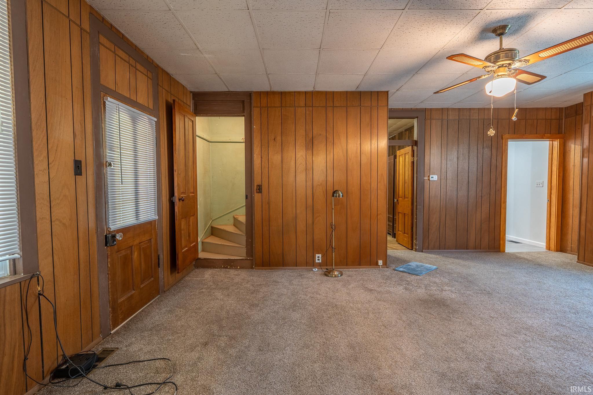 Interior space featuring wood paneling throughout, a ceiling fan with integrated lighting, and carpeted flooring