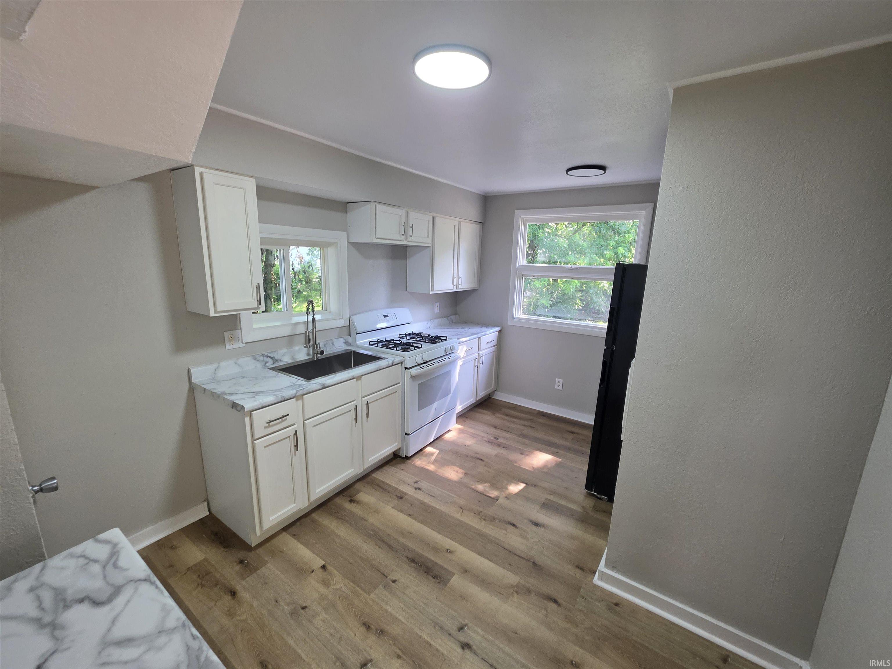 Kitchen featuring white cabinetry, wood-finish flooring, undermount sink with a gooseneck faucet, white range, and stone-look countertops
