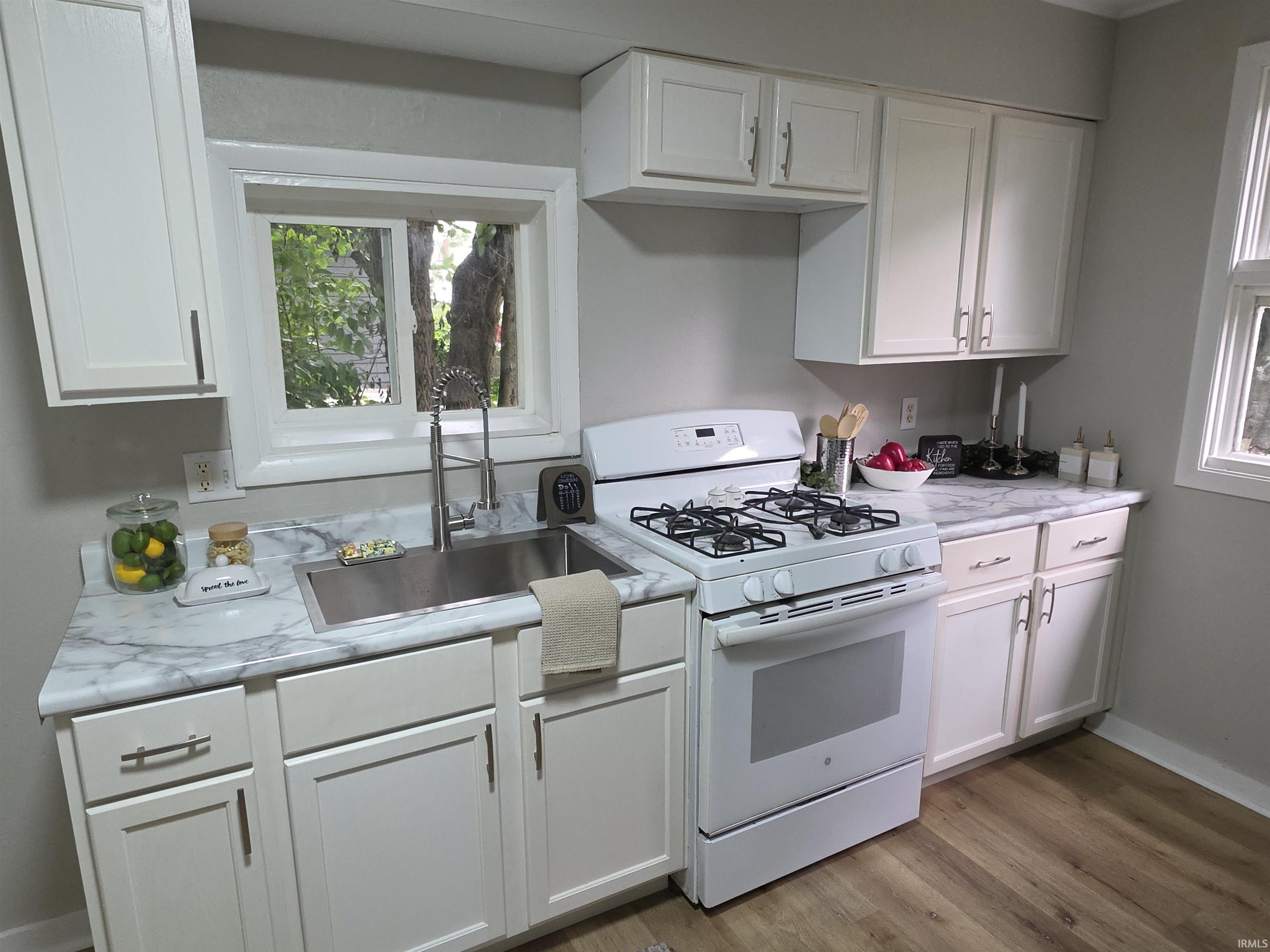 Kitchen featuring white cabinetry, a stainless steel sink with a gooseneck faucet, a white gas range, patterned countertops, and wood-finish flooring