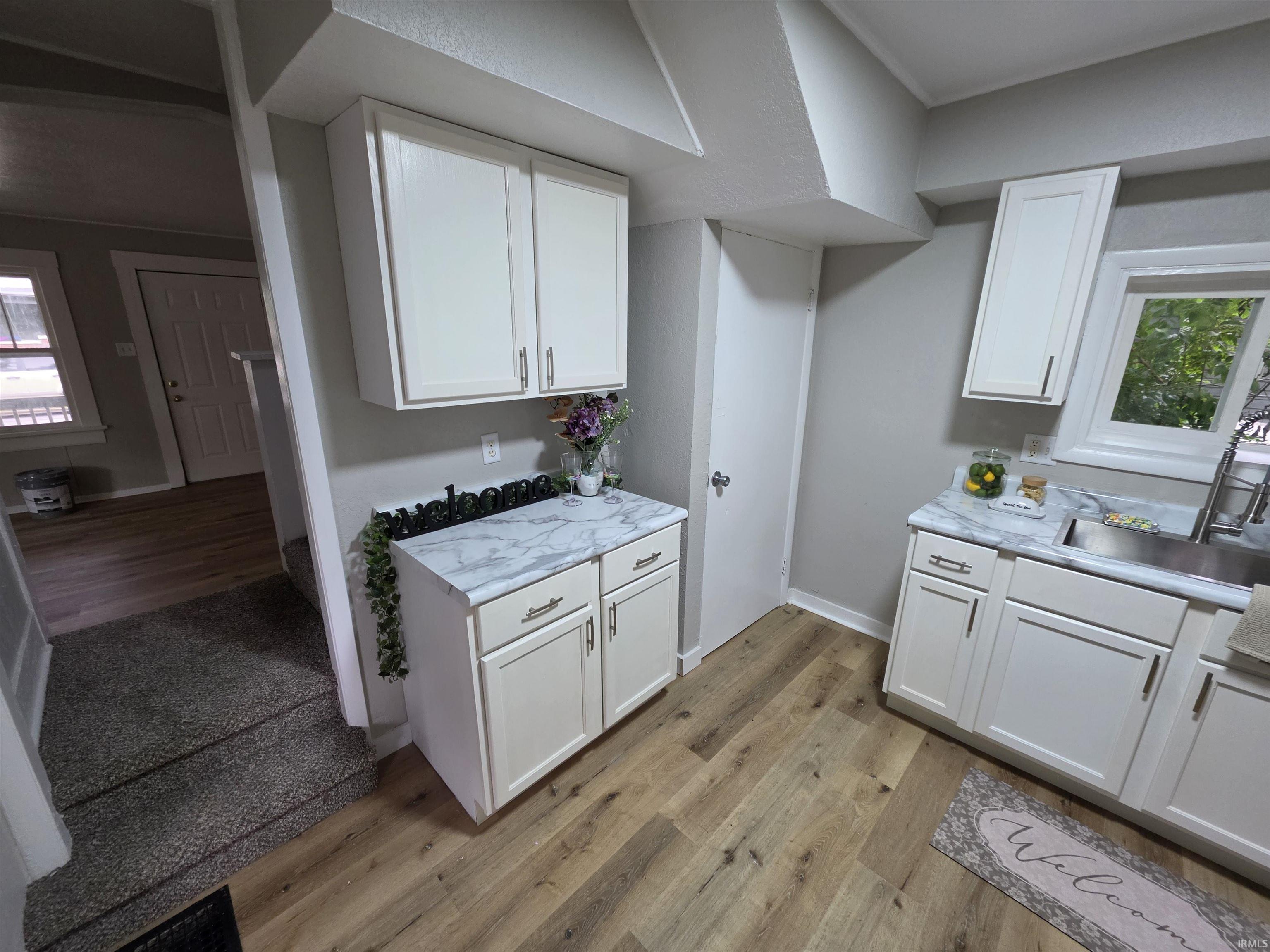 Kitchen area featuring crisp white cabinetry, marble-finish countertops, and wood-finish flooring