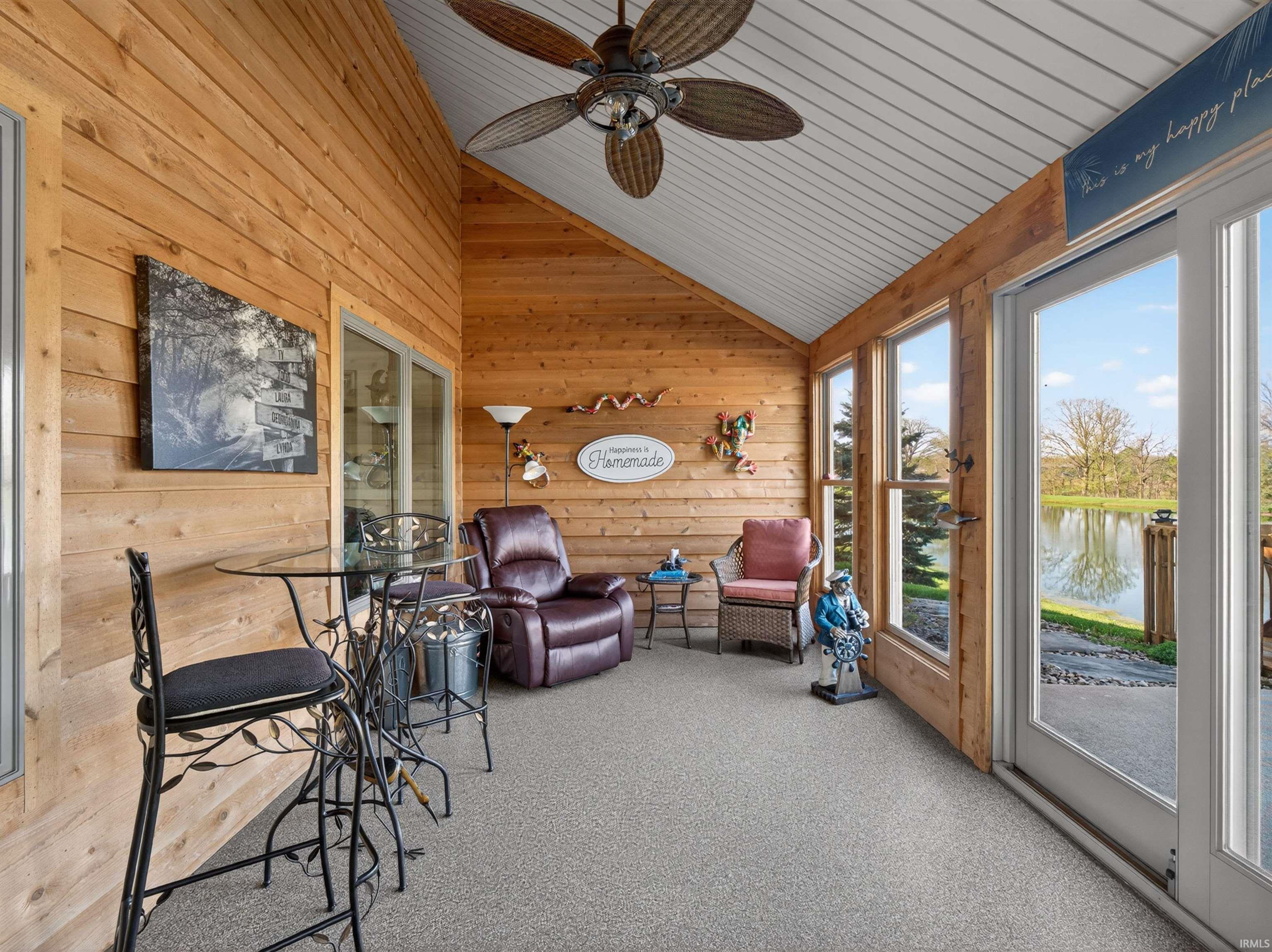 Sunroom SUNSCREEN ON PATIO DOOR AND WINDOWS reduces sunrays in afternoon. featuring natural cedar wood-paneled walls, a vaulted white ceiling, and a ceiling fan w/light