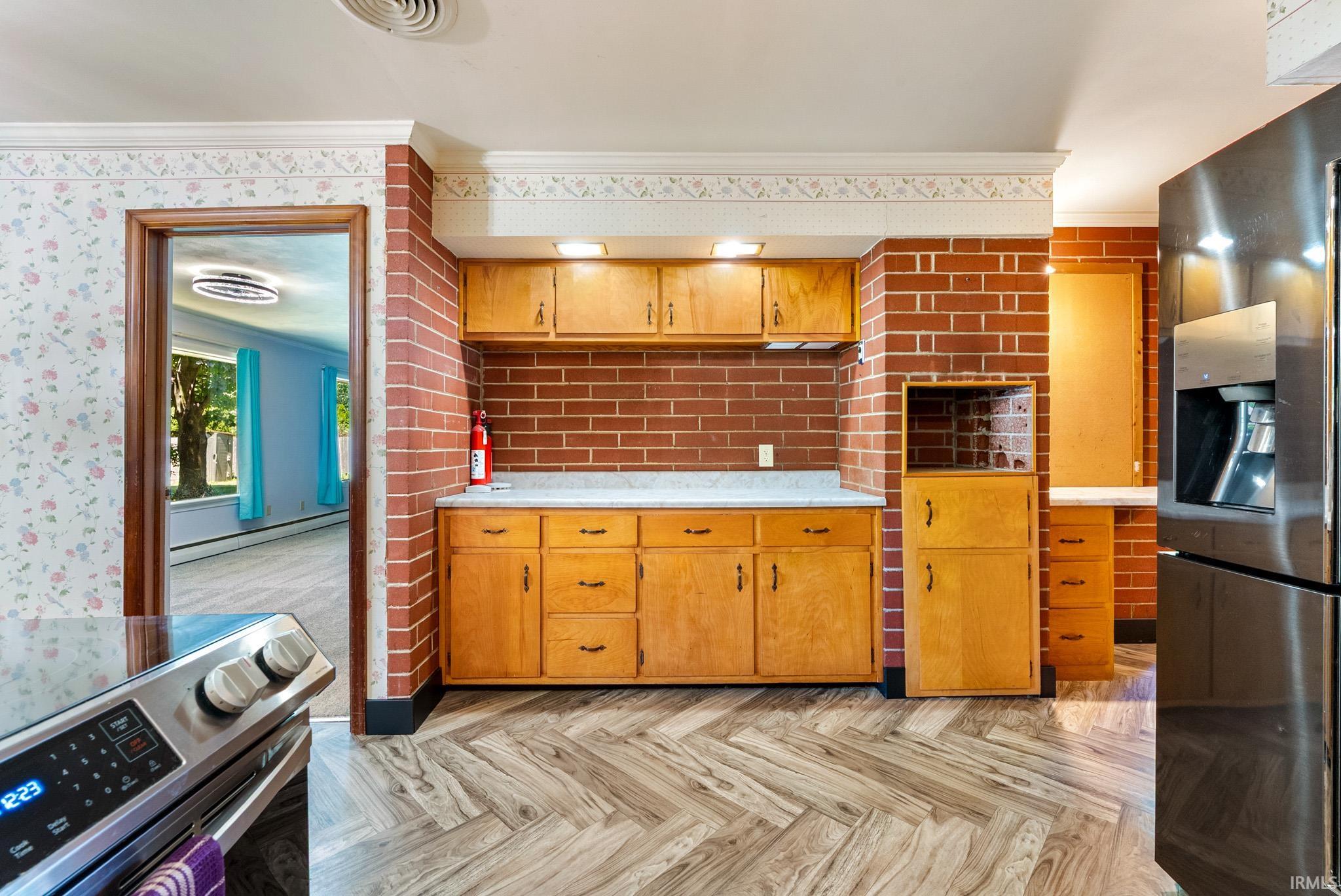 Kitchen featuring wood-finish flooring, brick accent walls, wood cabinetry, and light-toned countertops