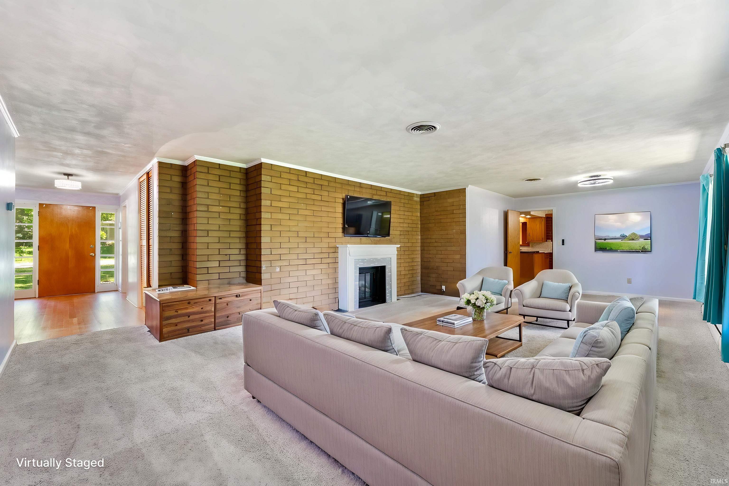 Spacious living area featuring a brick accent wall, a white fireplace with a mantel, and light-colored carpeting