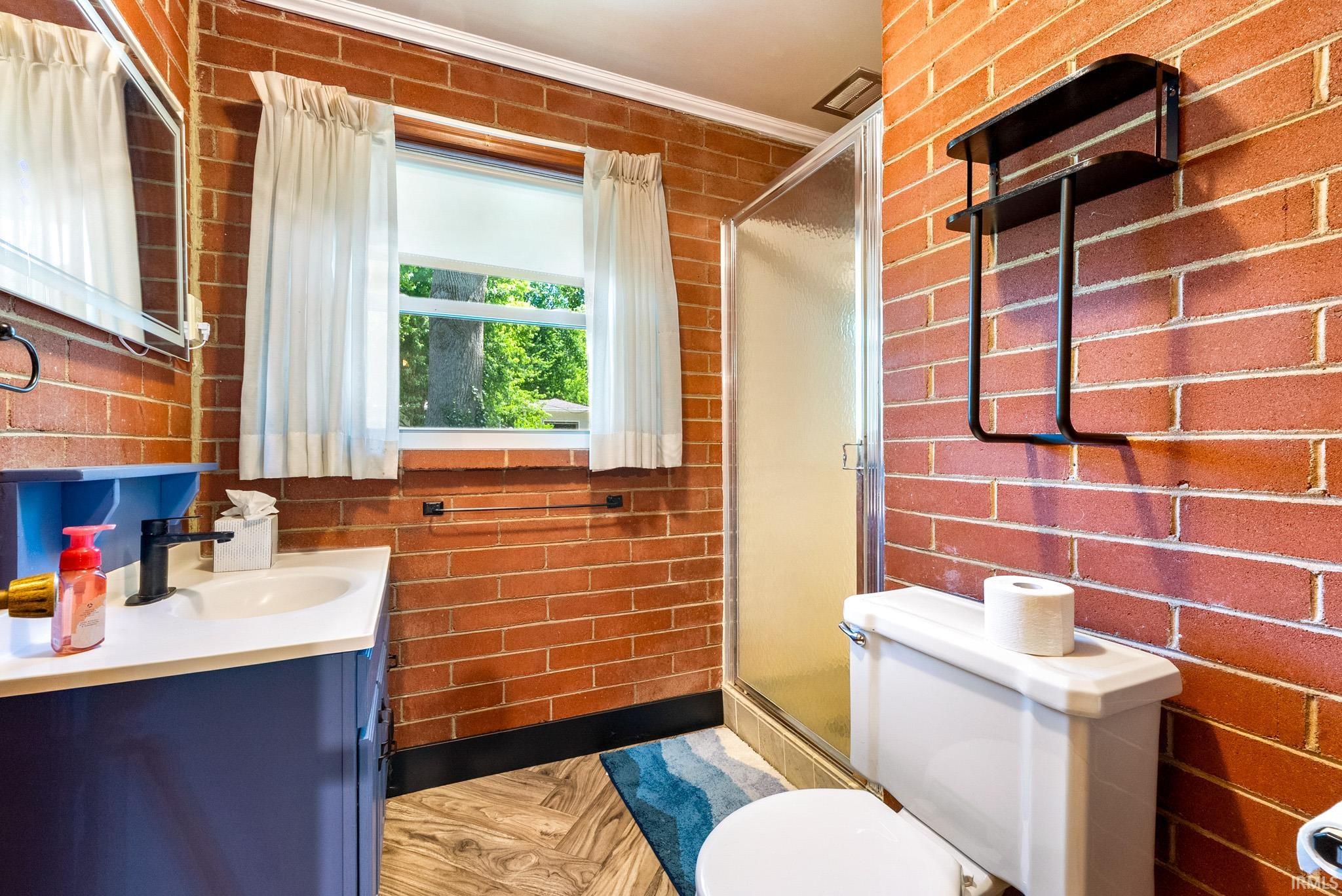 Bathroom featuring exposed brick walls, a white vanity with a rectangular sink, matte black faucet, and a glass-enclosed shower