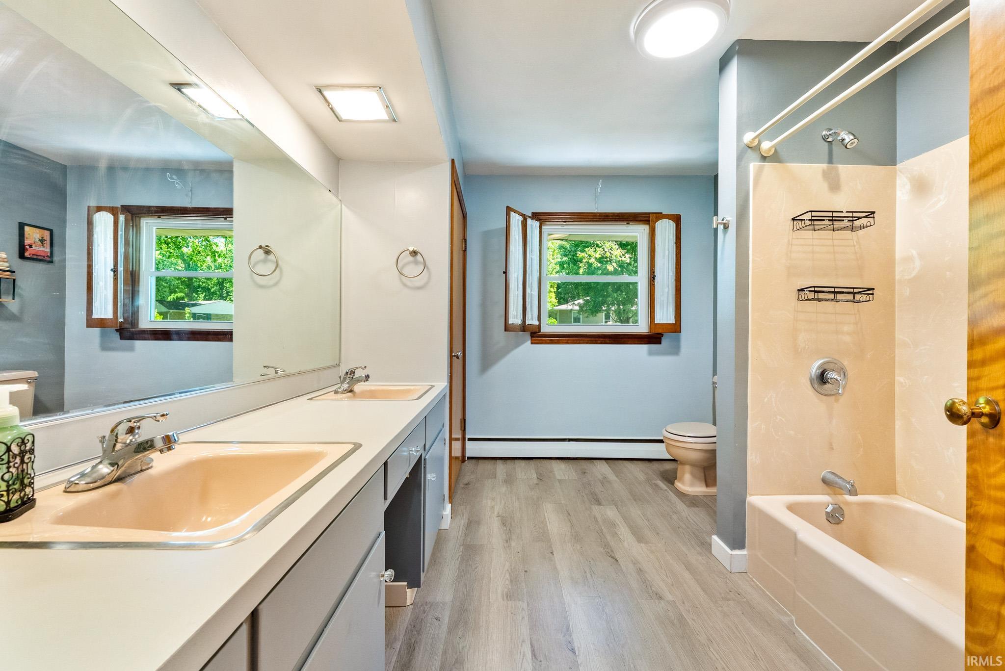 Bathroom featuring dual vanity with integrated sinks, a tub/shower combination, and wood-finish flooring