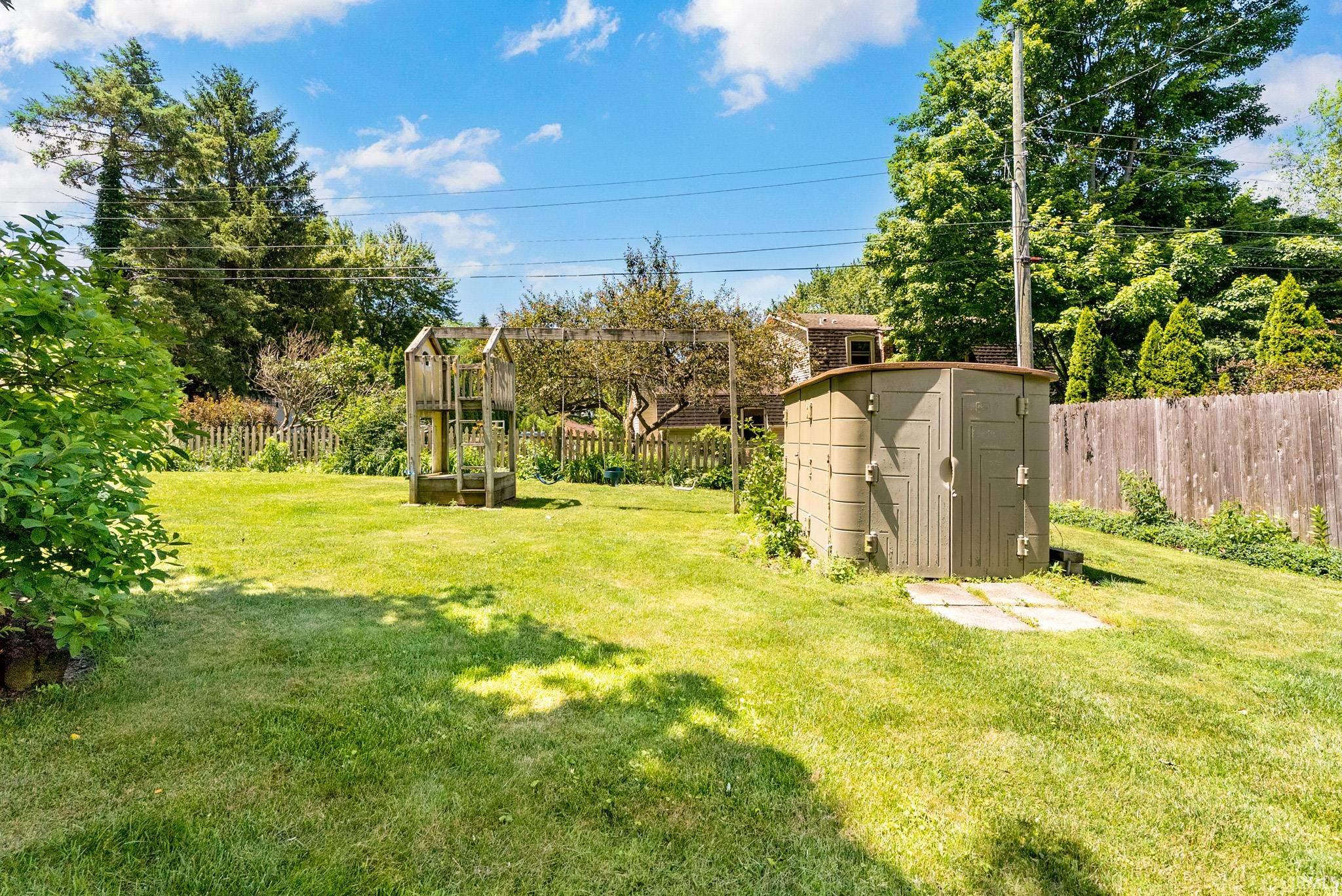 Expansive green lawn with mature trees and a built-in outdoor storage shed