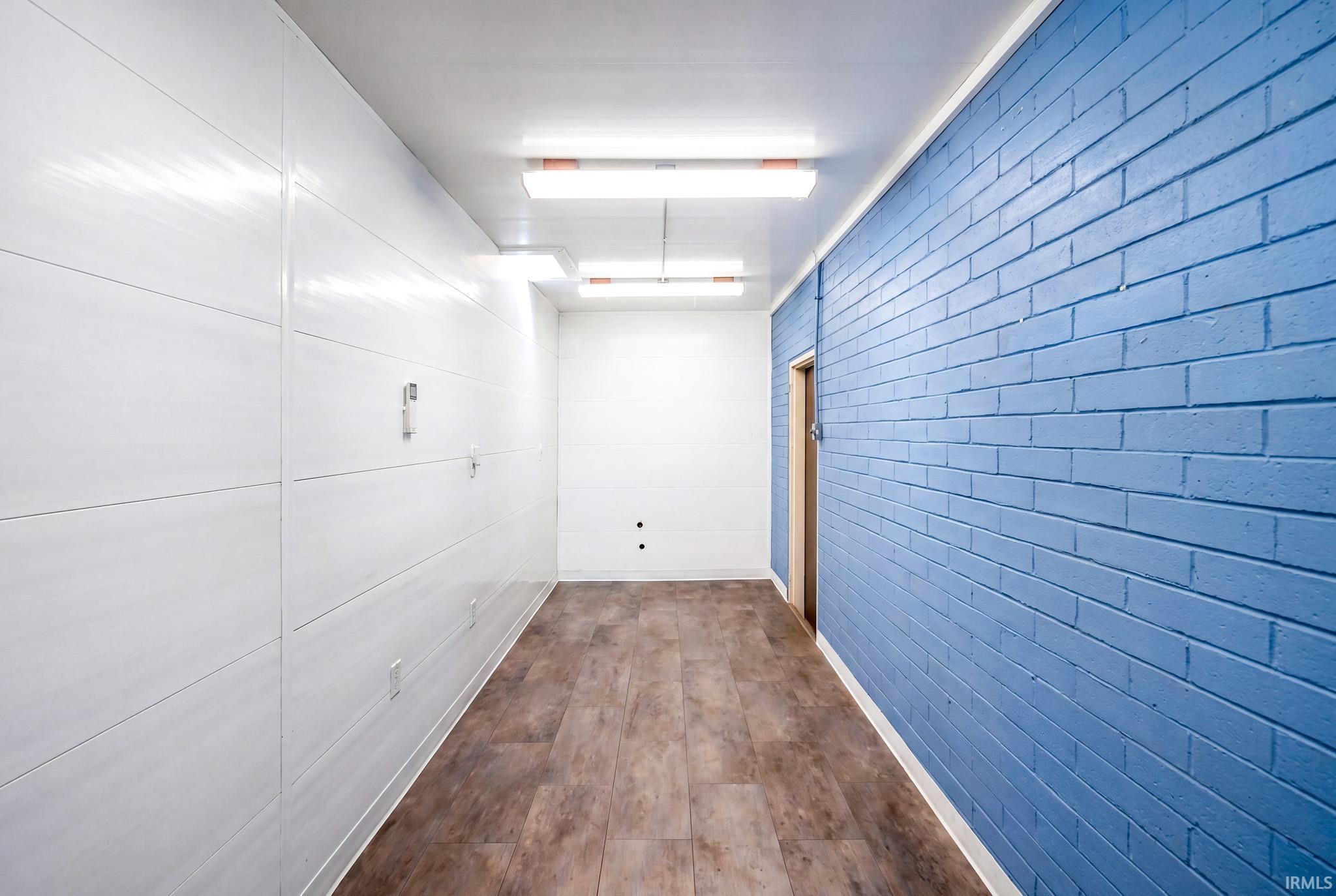Hallway featuring wood-finish flooring, a blue painted brick wall, and a white paneled wall
