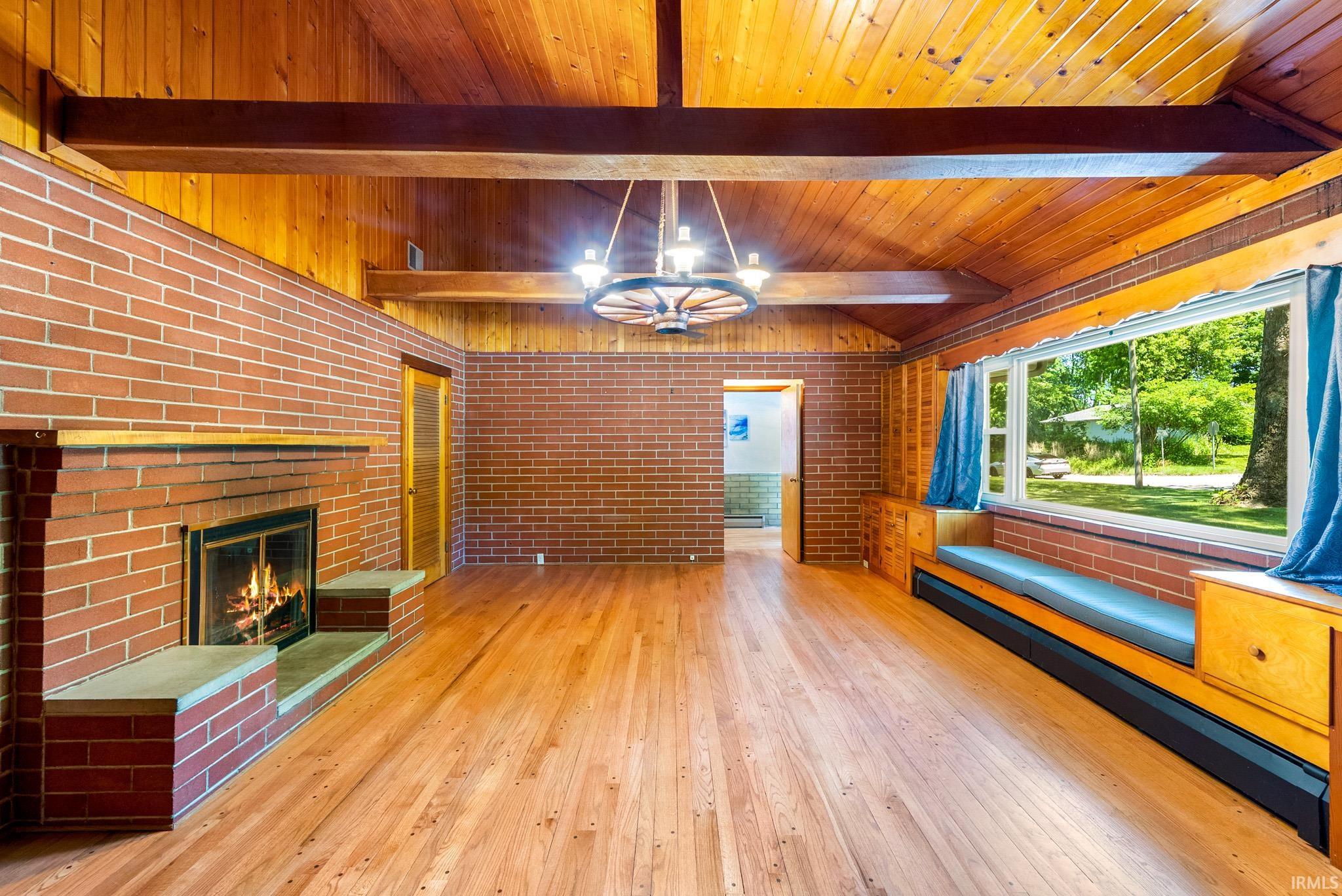 Living area featuring natural wood-finish flooring, exposed brick walls, and a prominent brick fireplace with hearth