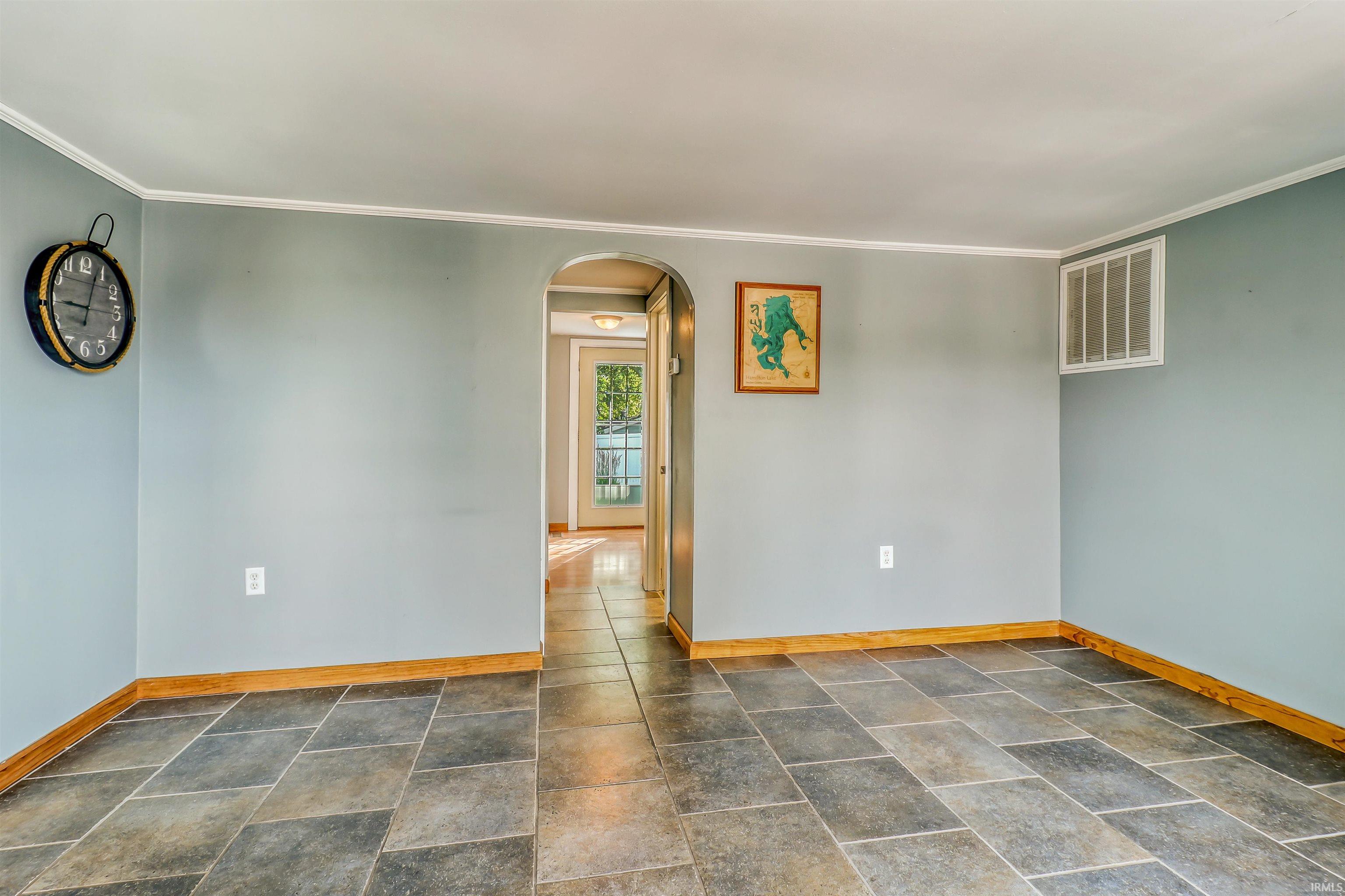 Spacious room featuring slate-look tile flooring, light blue wall paint, white crown molding, and wooden baseboards