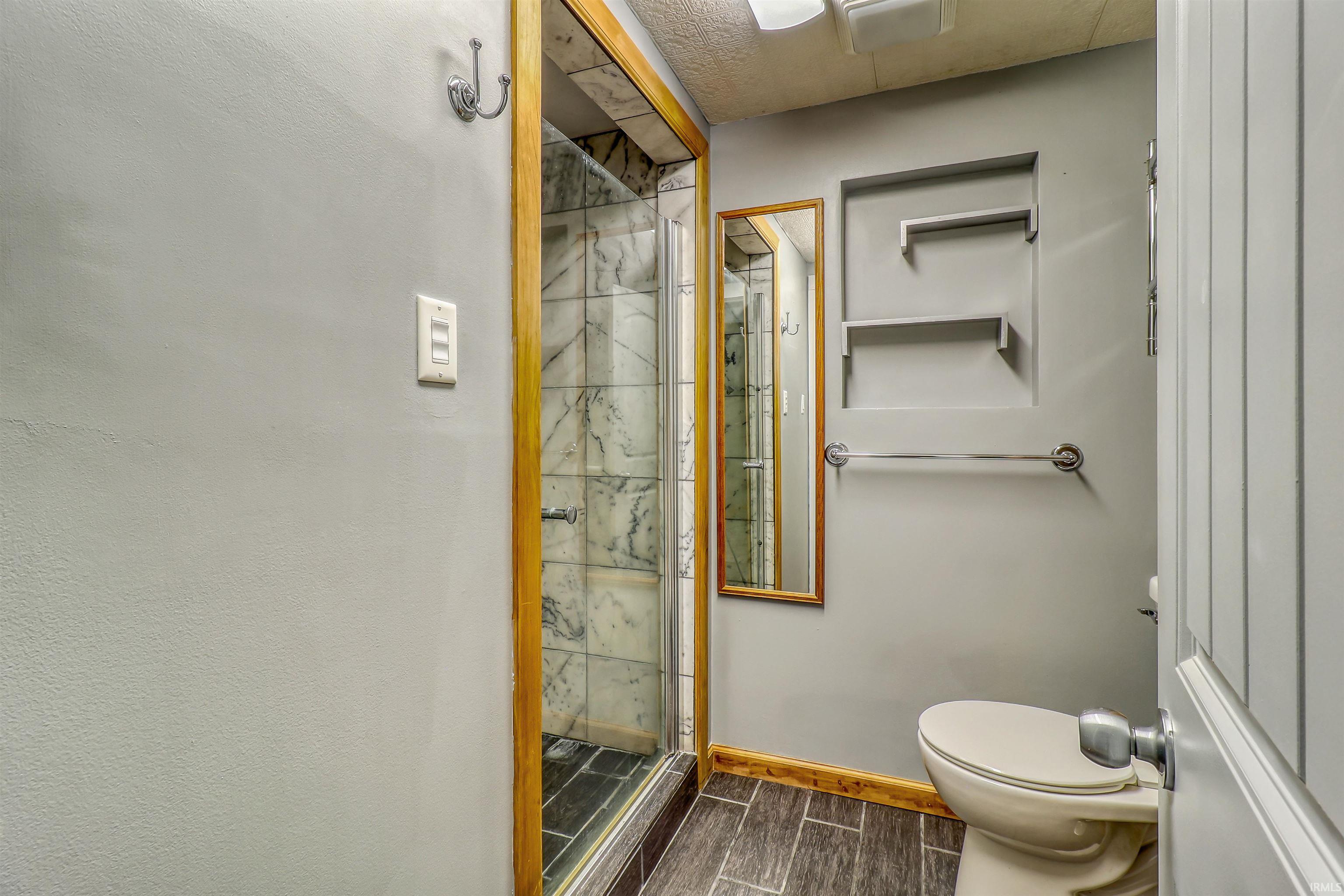 Compact bathroom featuring a glass-enclosed shower with marble-look tile surround and dark tile flooring