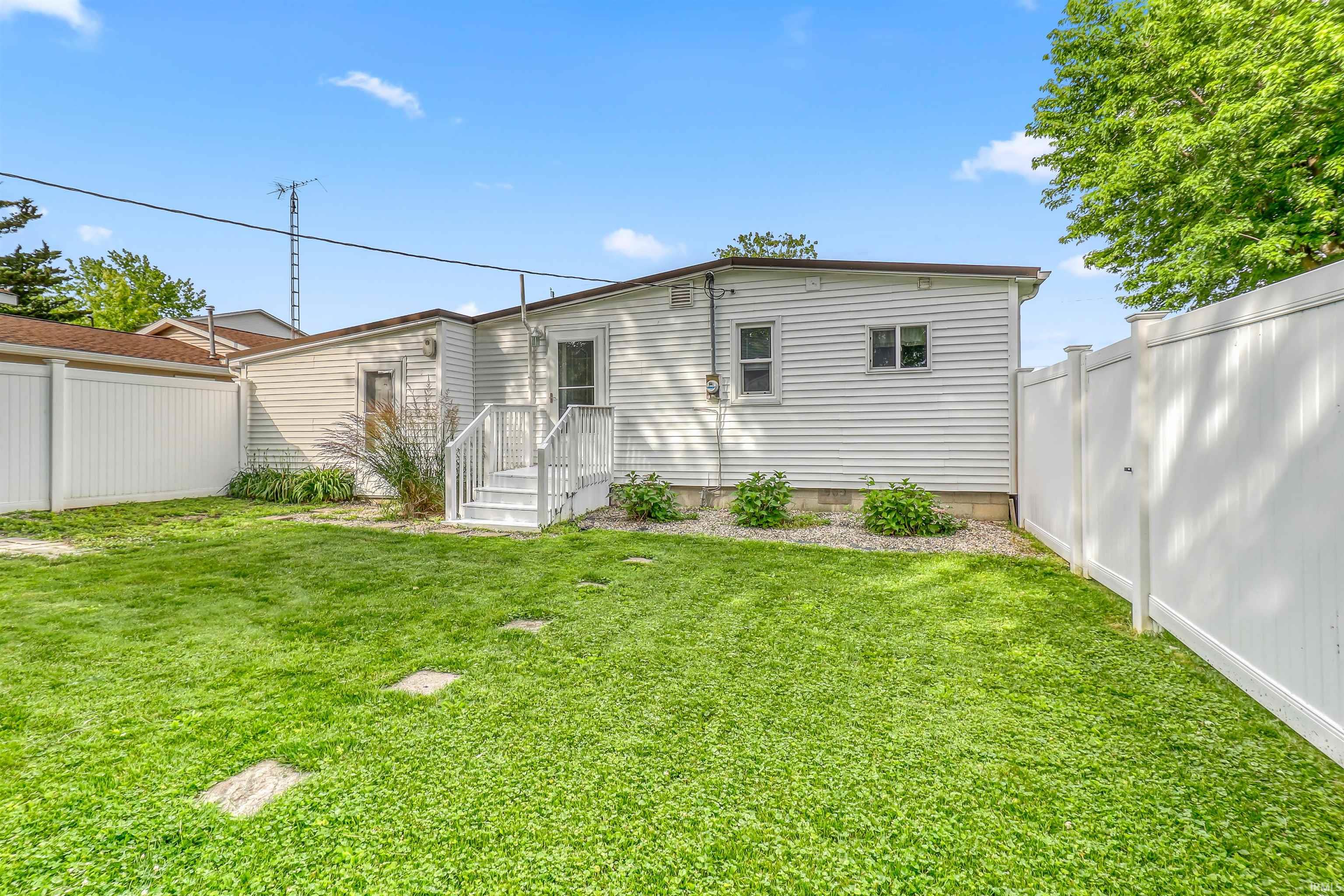 Grassy yard featuring white vinyl fencing and a white sided structure with a small deck and stairs