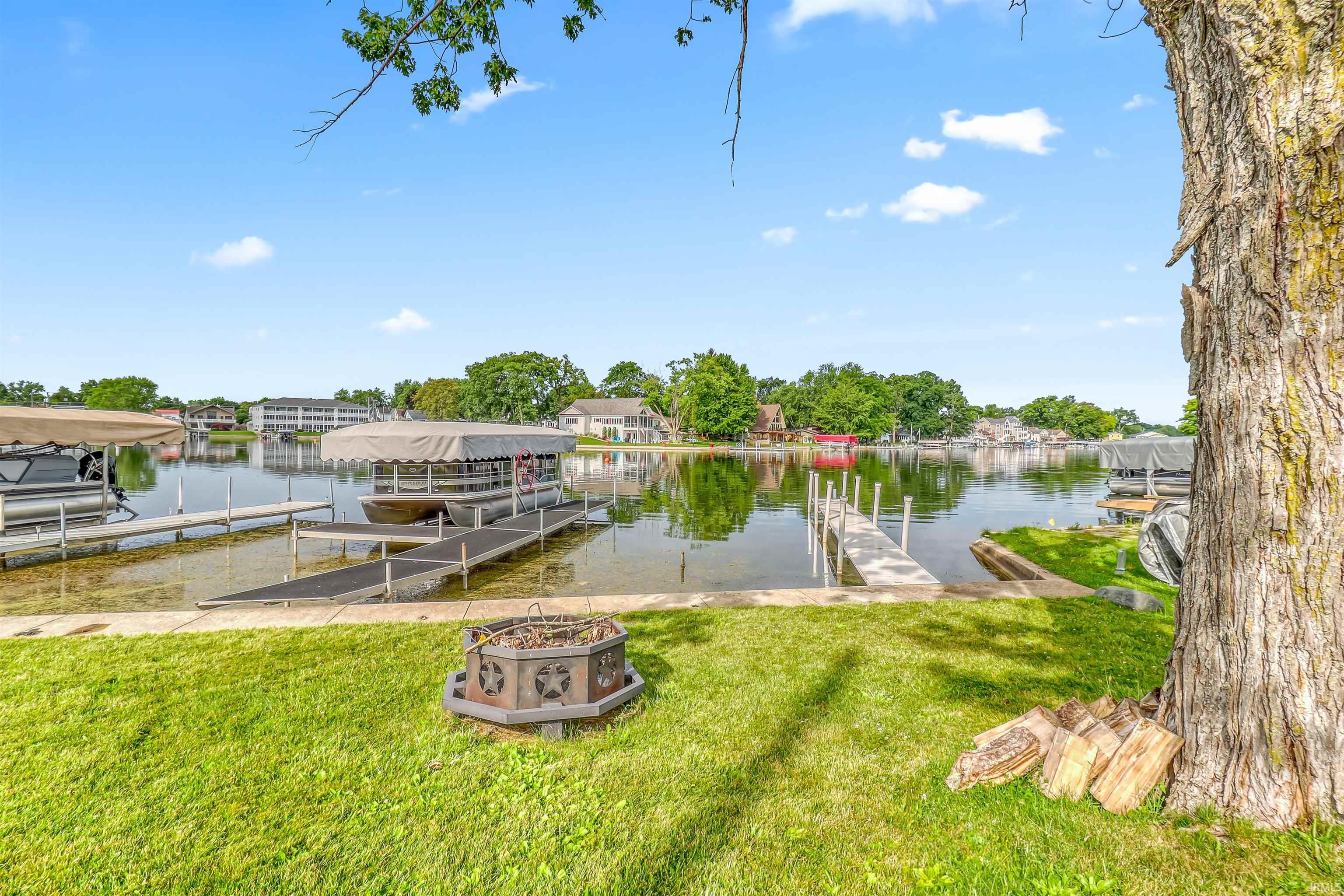 Expansive waterfront property featuring a manicured lawn, multiple boat docks, and a built-in fire pit