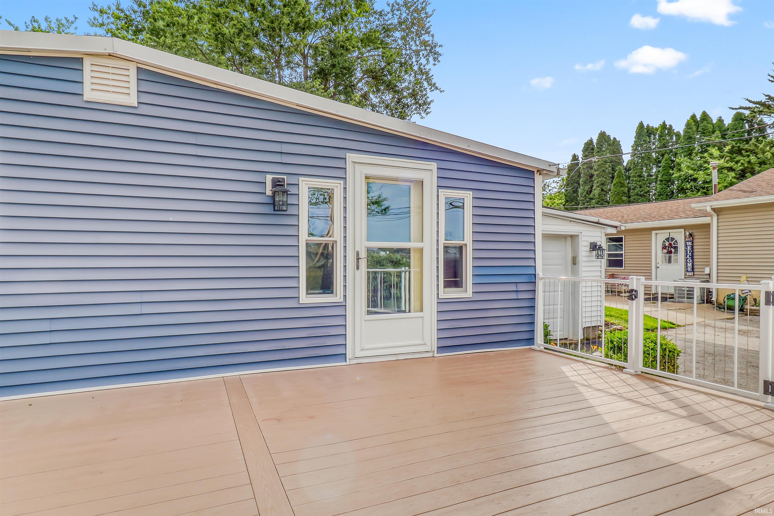 Expansive outdoor deck featuring wood-finish flooring, a white metal fence, and a blue siding exterior with a white door