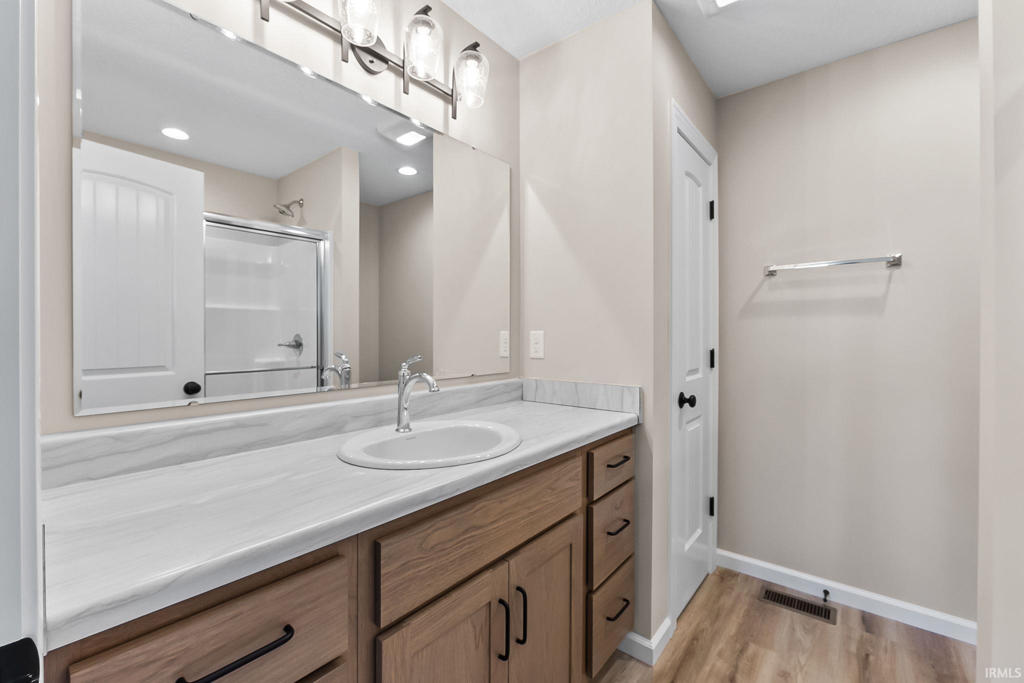 Bathroom featuring a spacious wood-finish vanity with an integrated sink, a large wall-mounted mirror, and a contemporary light fixture