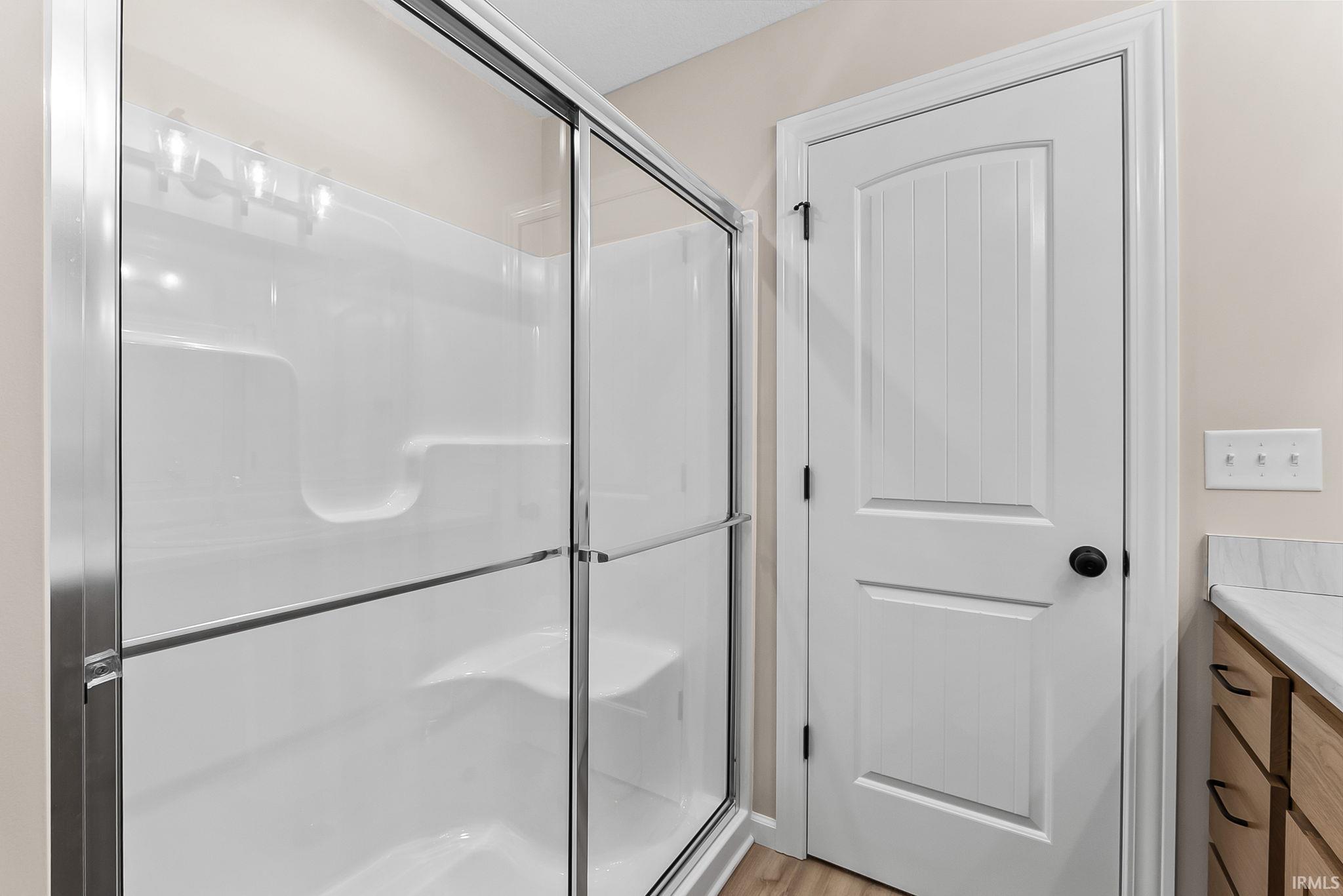 Shower with clear glass sliding doors and integrated shelving, alongside a white paneled door with black hardware