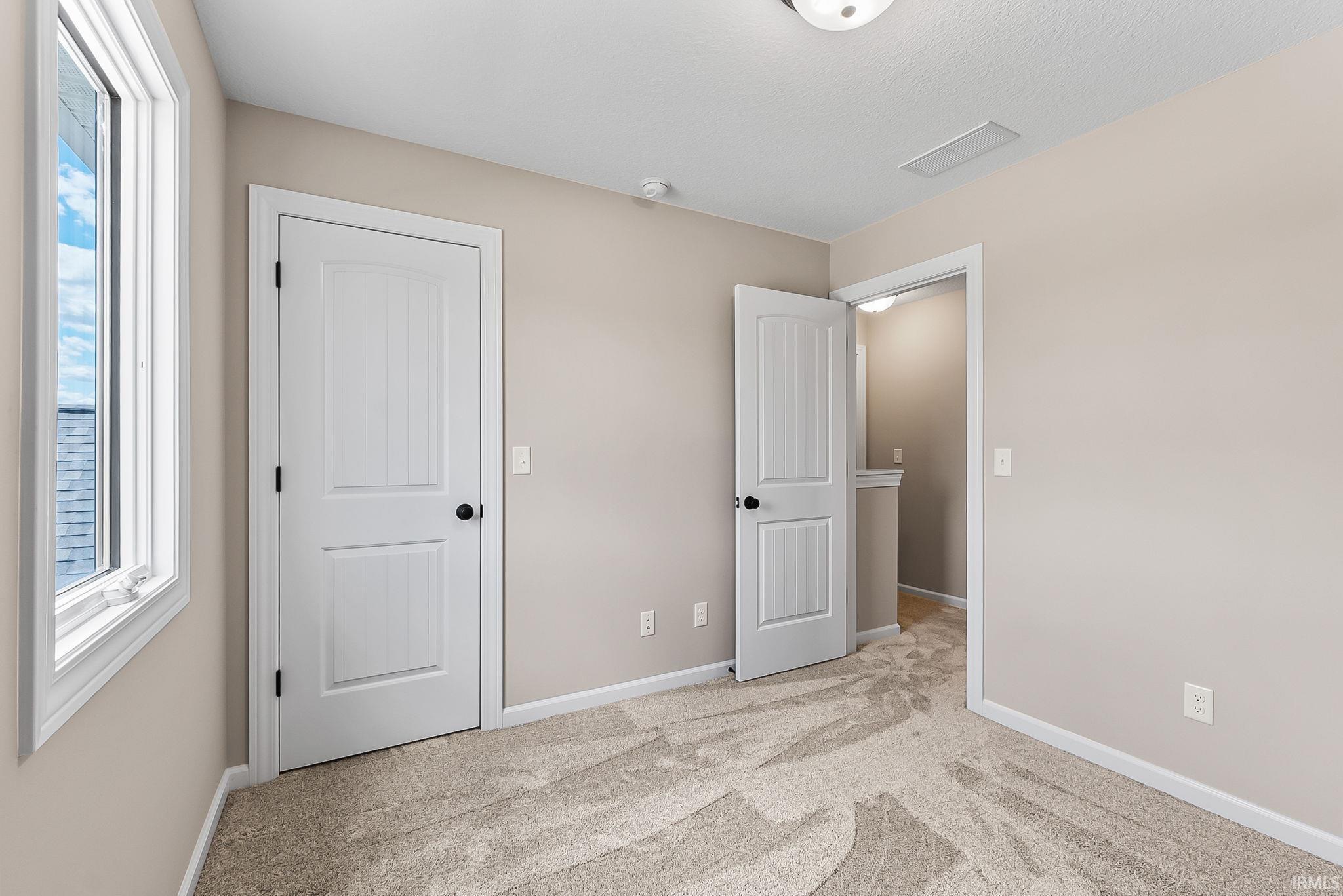 Neutral tone wall paint with white trim, new carpet flooring, and two paneled doors with matte black hardware